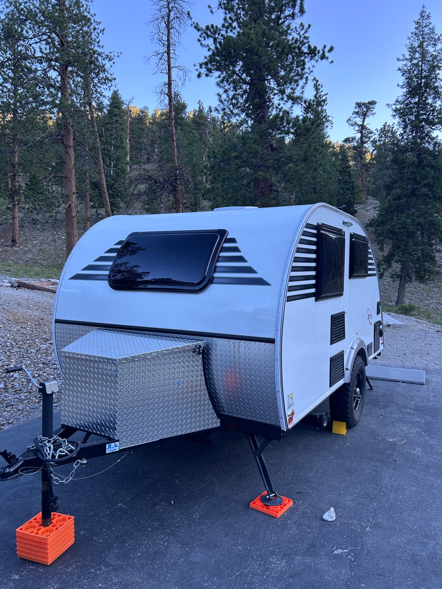 A compact rv rental, a white teardrop trailer, parked in a tranquil pine forest campsite for a nature getaway.
