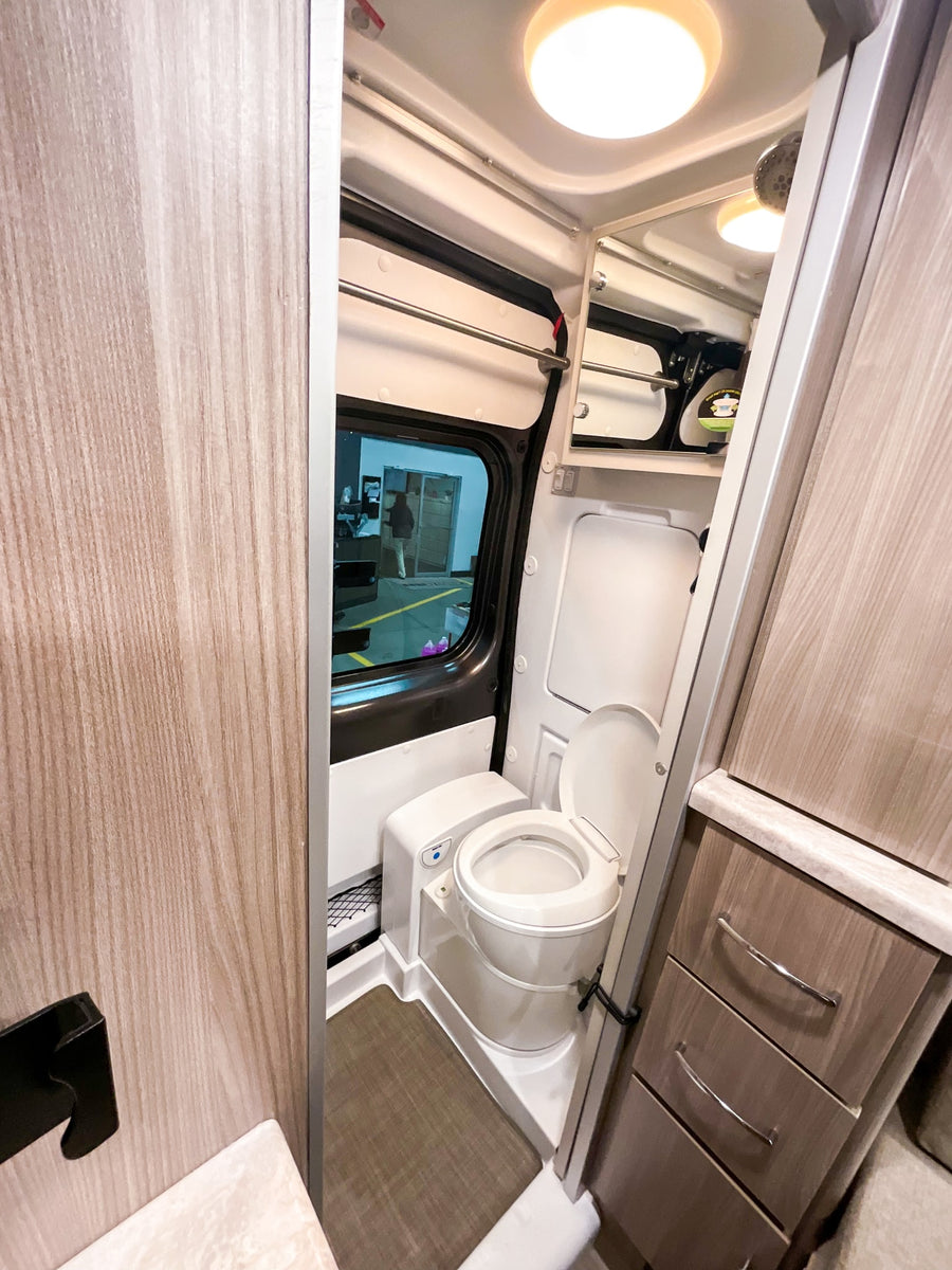 Compact RV rental bathroom with toilet, shower, and built-in storage, perfect for travel comfort.