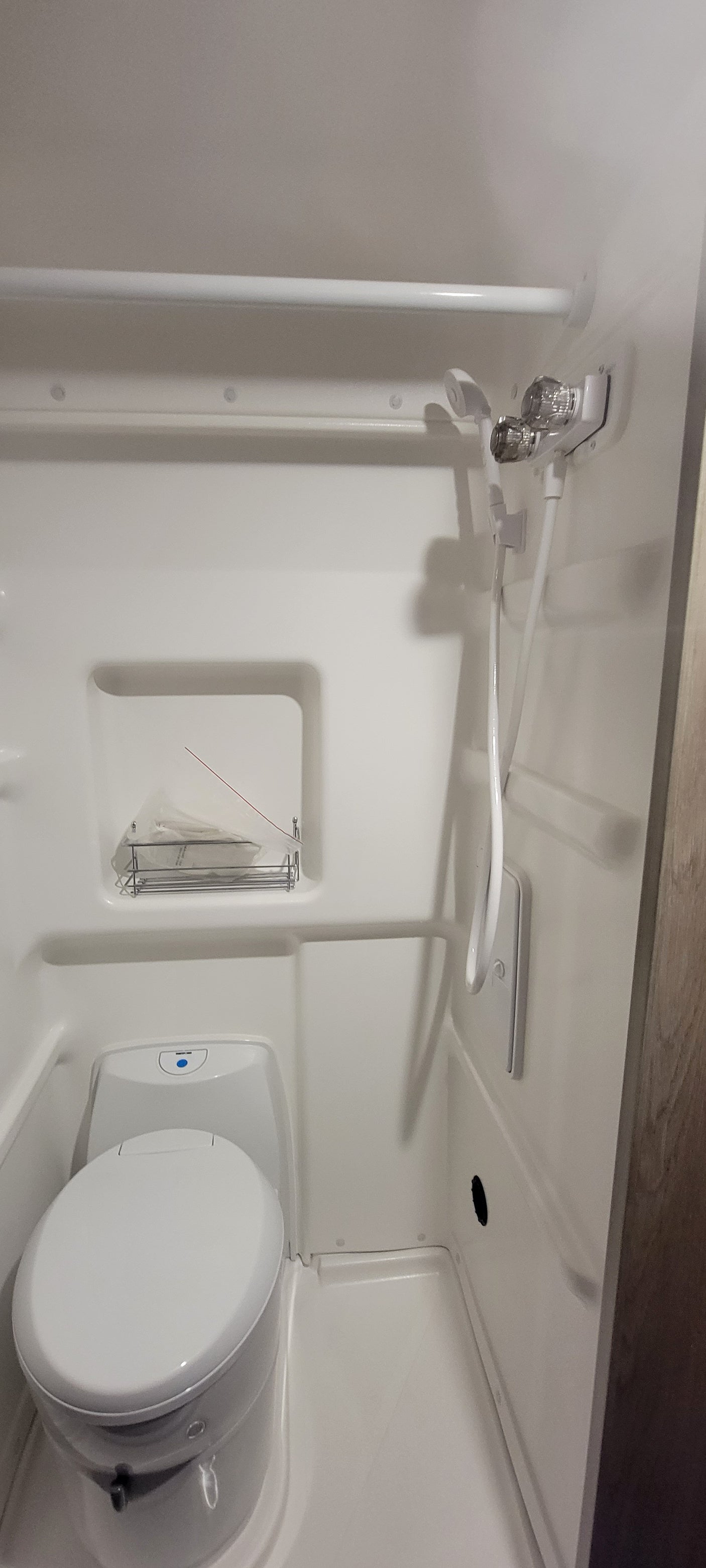 Interior of a compact, all-white RV rental bathroom, showing the shower and toilet setup.