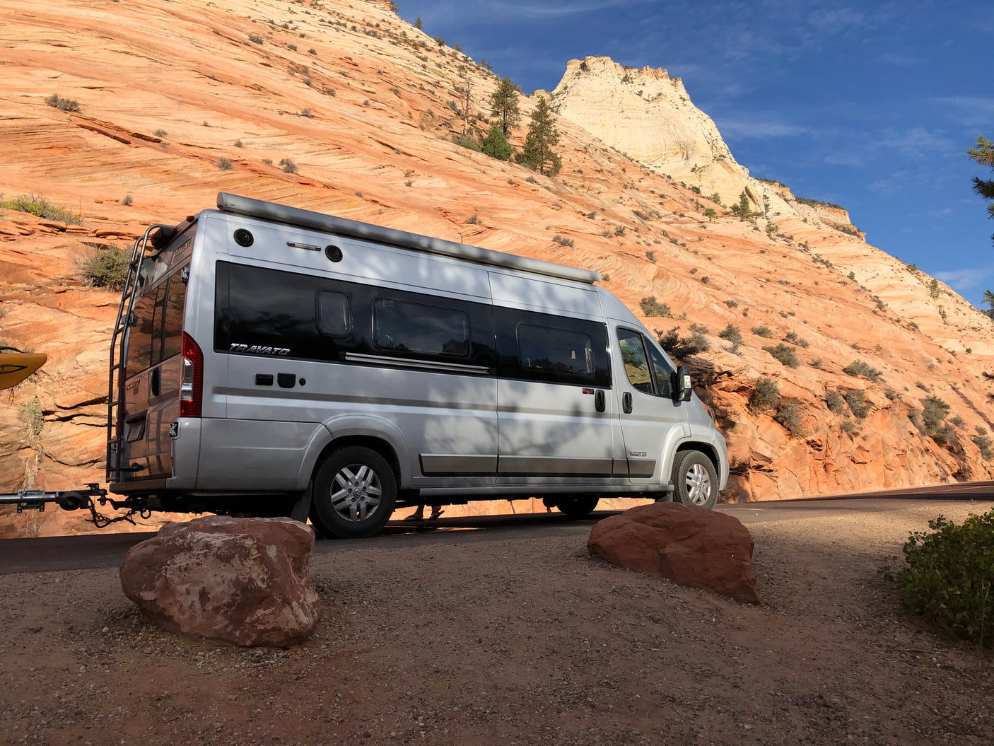 Winnebago Travato RV rental at a scenic pull-off. Silver van, red rock mountains, blue sky, and a kayak.