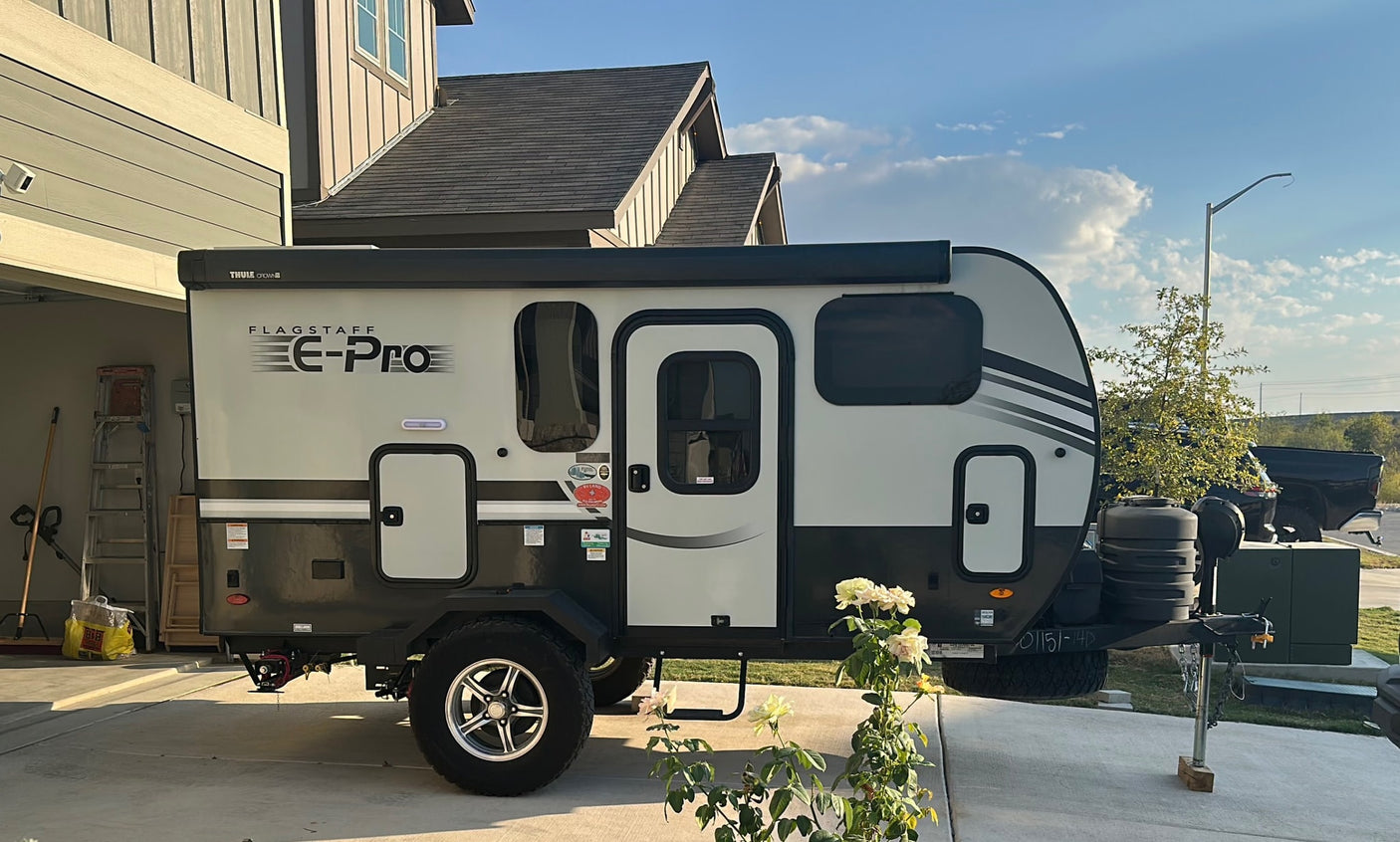 A Flagstaff E-Pro RV rental is parked with a Ford Bronco in a sunny driveway, ready for adventure.