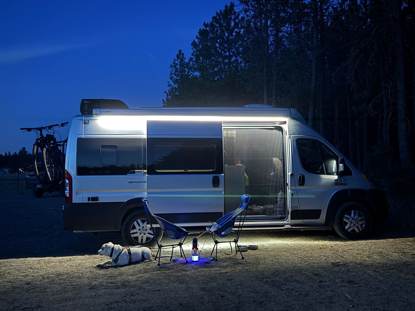 Night at a Sequoia RV rental campsite: van, resting dog, chairs, and lantern. Perfect for outdoor adventures.