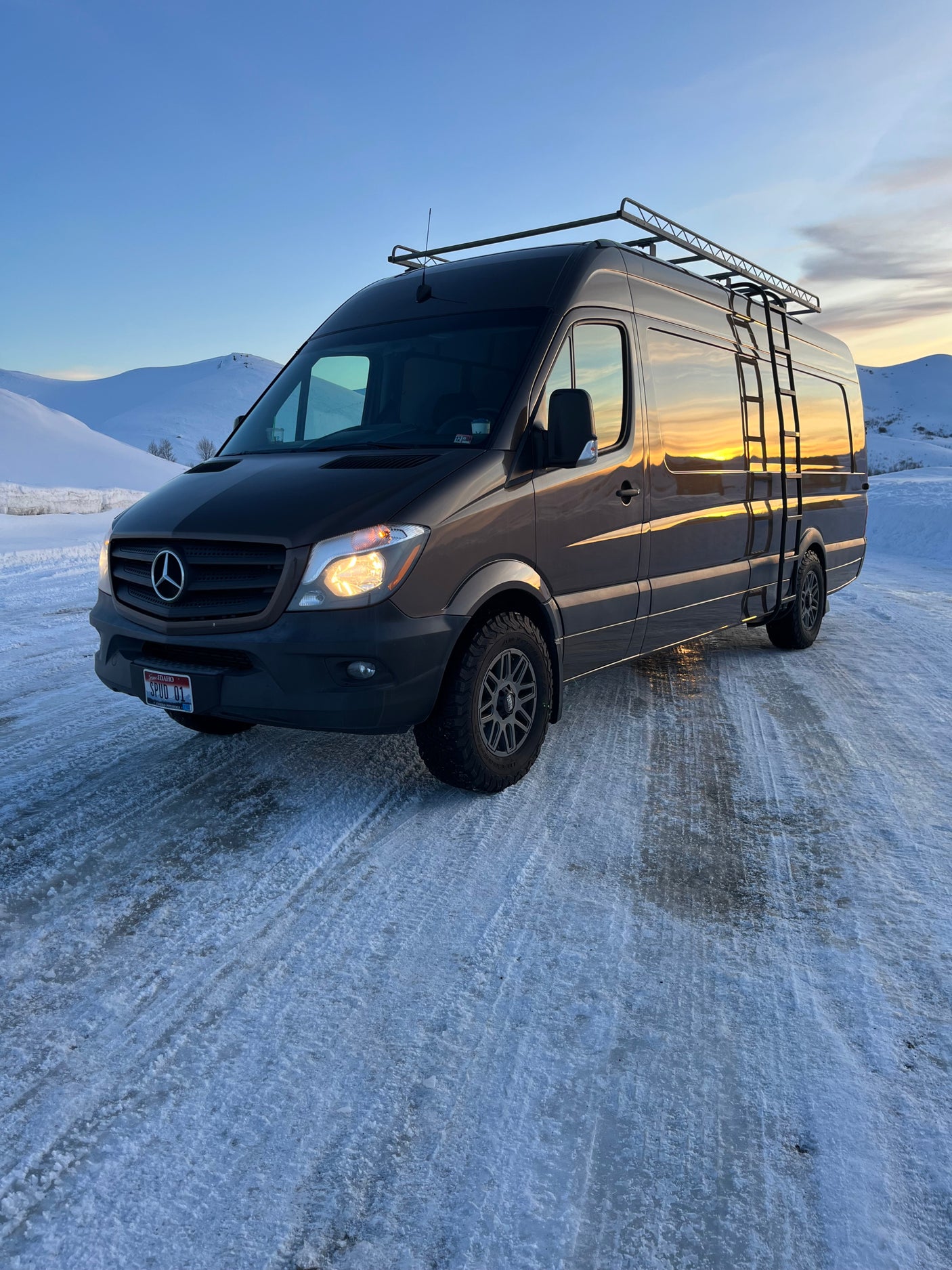 RV rental: Dark grey Mercedes Sprinter van, equipped for winter mountain adventures, parked on a snowy road.