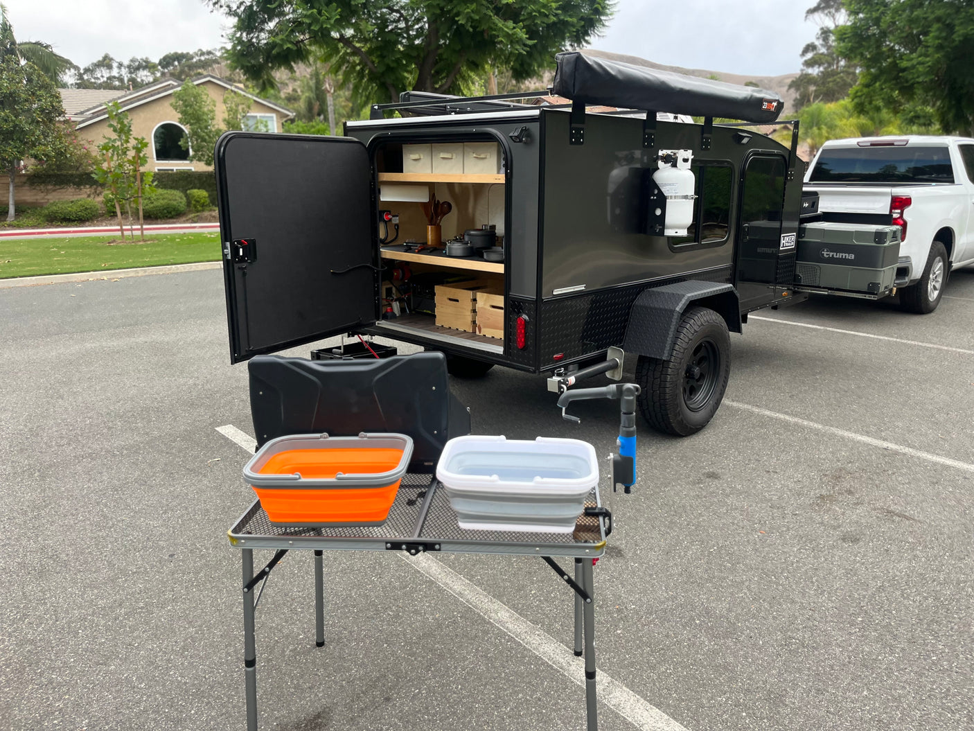 RV rental: Compact overland camper trailer with outdoor kitchen, wash basins, and attached pickup truck, parked in a lot.