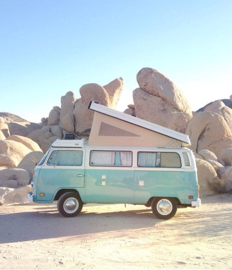 Light blue VW camper van with pop-top roof in rocky desert. Perfect for a unique RV rental adventure or road trip van life camping.