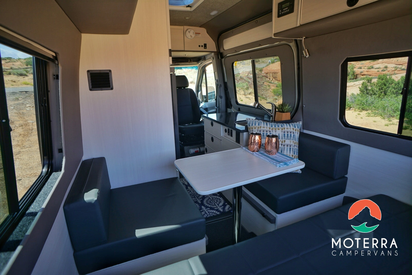 Modern campervan RV rental interior featuring a dinette, compact kitchen, comfy seating, and scenic views.