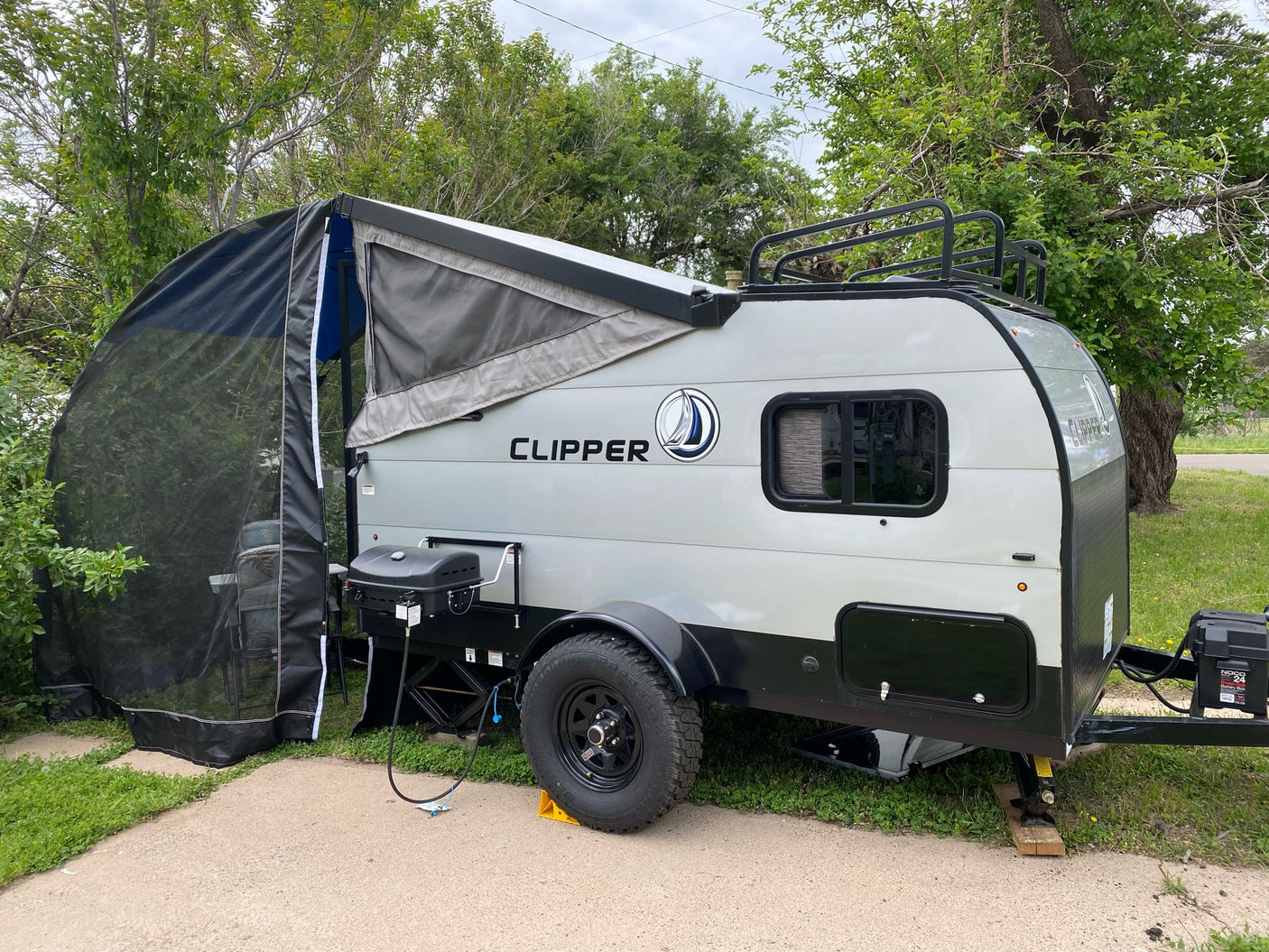 parked under a cloudy sky.|RV rental: Compact Clipper pop-up camper with screen room and grill