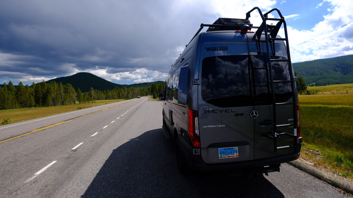 Winnebago Revel Sprinter RV rental parked on a scenic road, surrounded by mountains and forests under a dramatic sky.