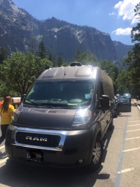 A grey Ram ProMaster camper van RV rental parked in a scenic mountain valley. Ideal for outdoor adventures.