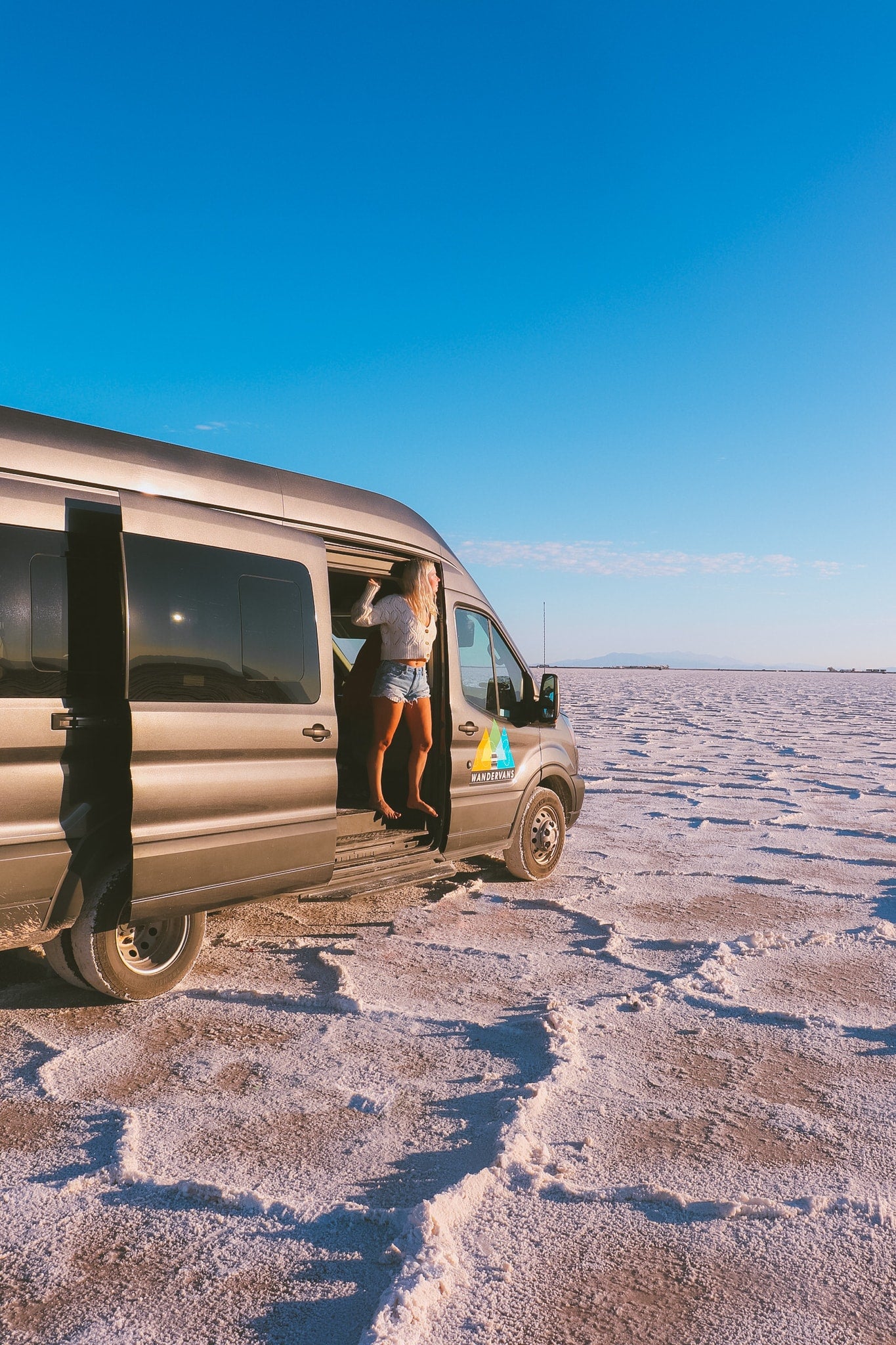 Explore vast landscapes! Woman steps out of her gray RV rental van onto salt flats under a clear sky.