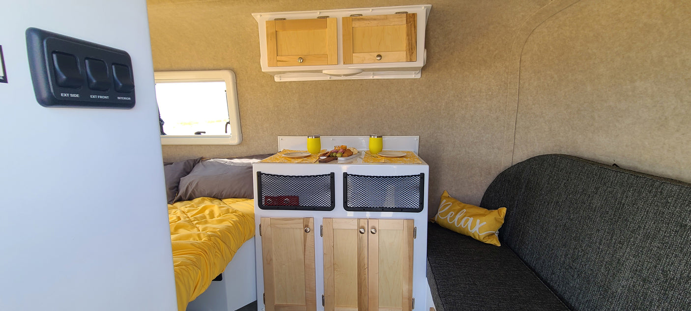 Inside an RV rental: a bright yellow bed, compact kitchen with snacks, and a comfortable sofa. Perfect for a cozy getaway.