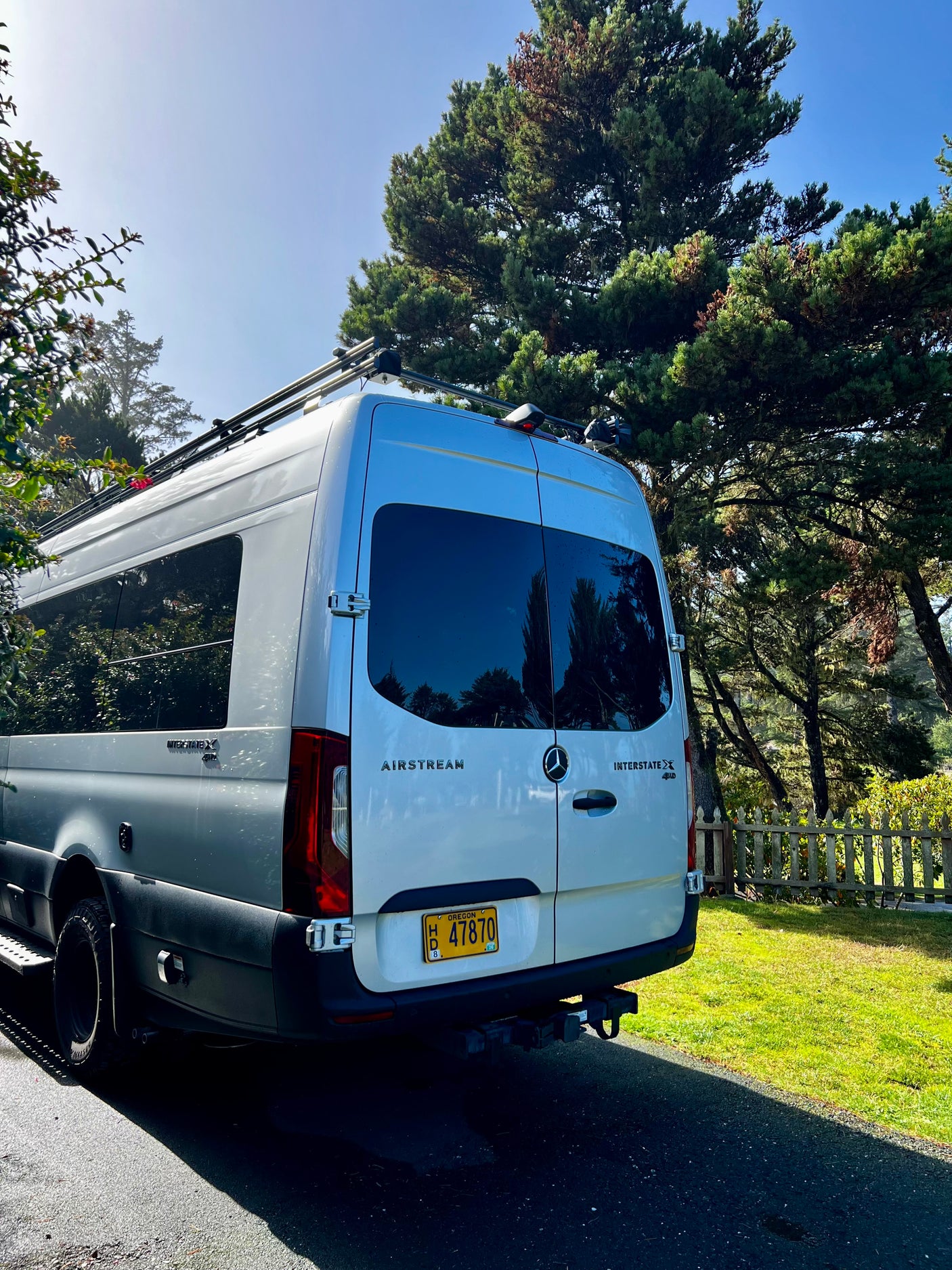 White Airstream Interstate X 4x4 rv rental, ideal for outdoor travel. Parked on asphalt with trees & grass in the sun.