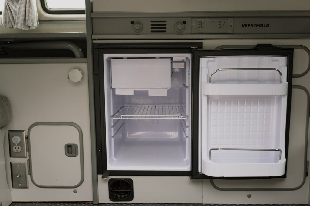 Spotless open RV rental refrigerator in a camper van interior, with controls visible. Perfect for your next road trip or camping adventure.