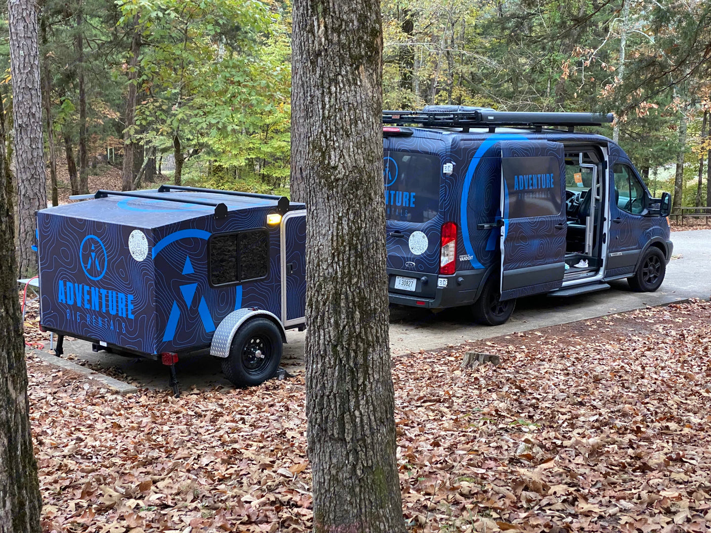 Adventure RV rental van & matching trailer parked in autumn woods.