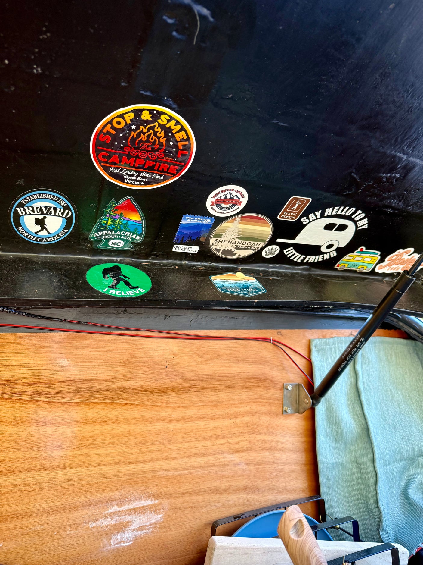 RV rental interior: A collection of outdoor adventure stickers, including National Parks & camping, on a dark surface above a wooden panel.