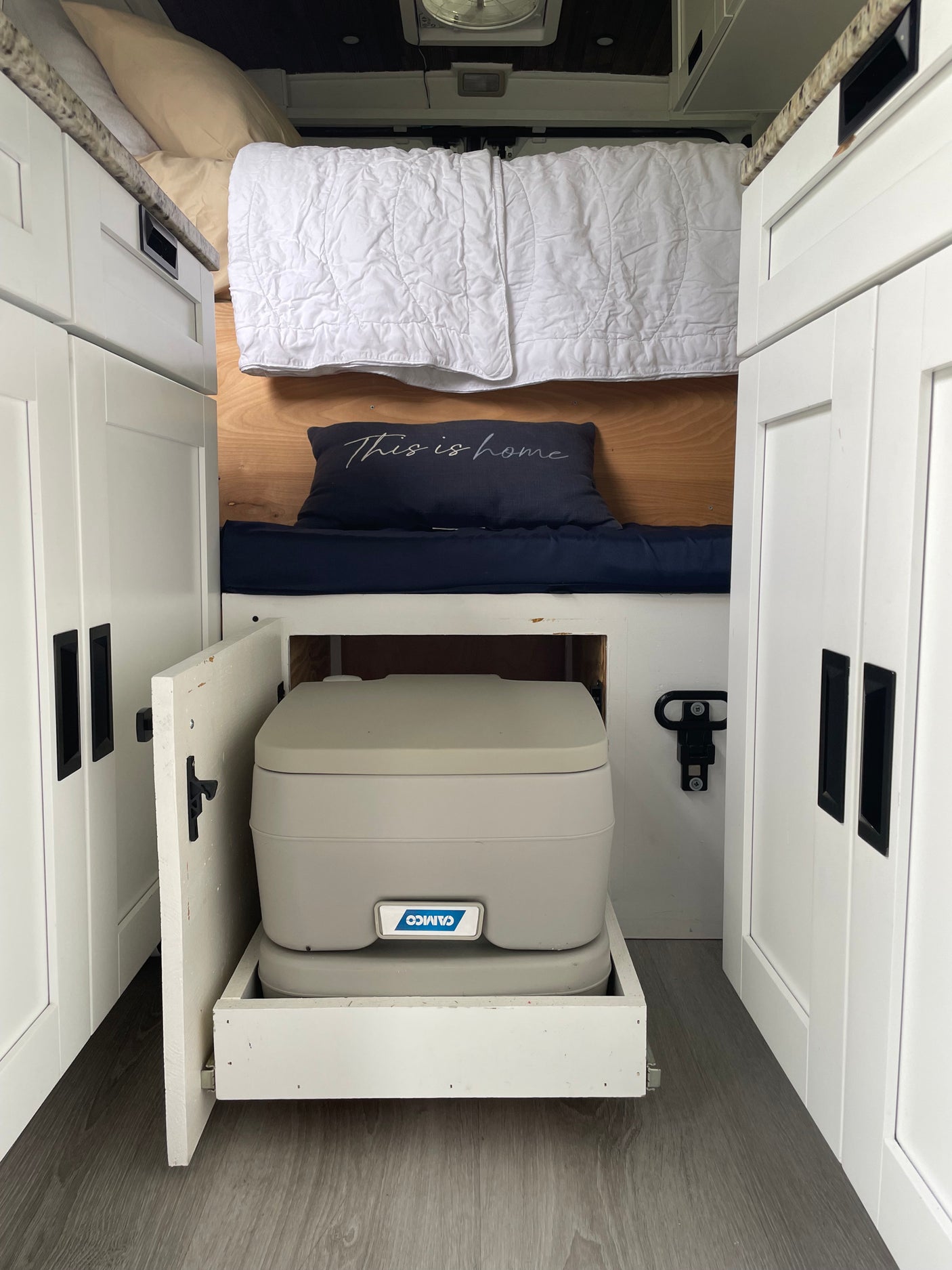 RV rental interior: Bed, white cabinets, and a pull-out portable toilet. Compact, functional design for life on the road.