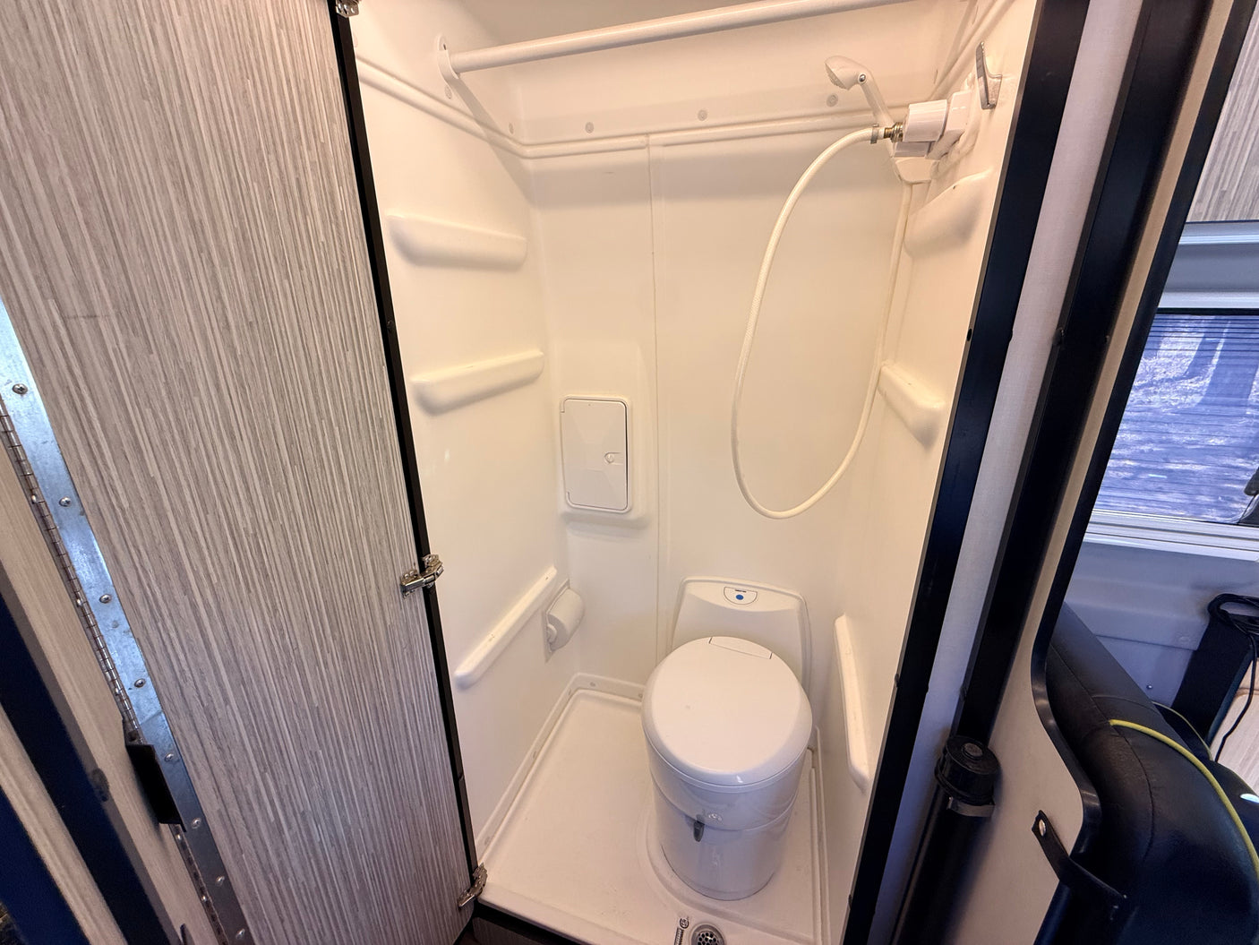 A compact, all-in-one wet bath in an RV rental, featuring a toilet, handheld showerhead, and small shelves within the shower stall.