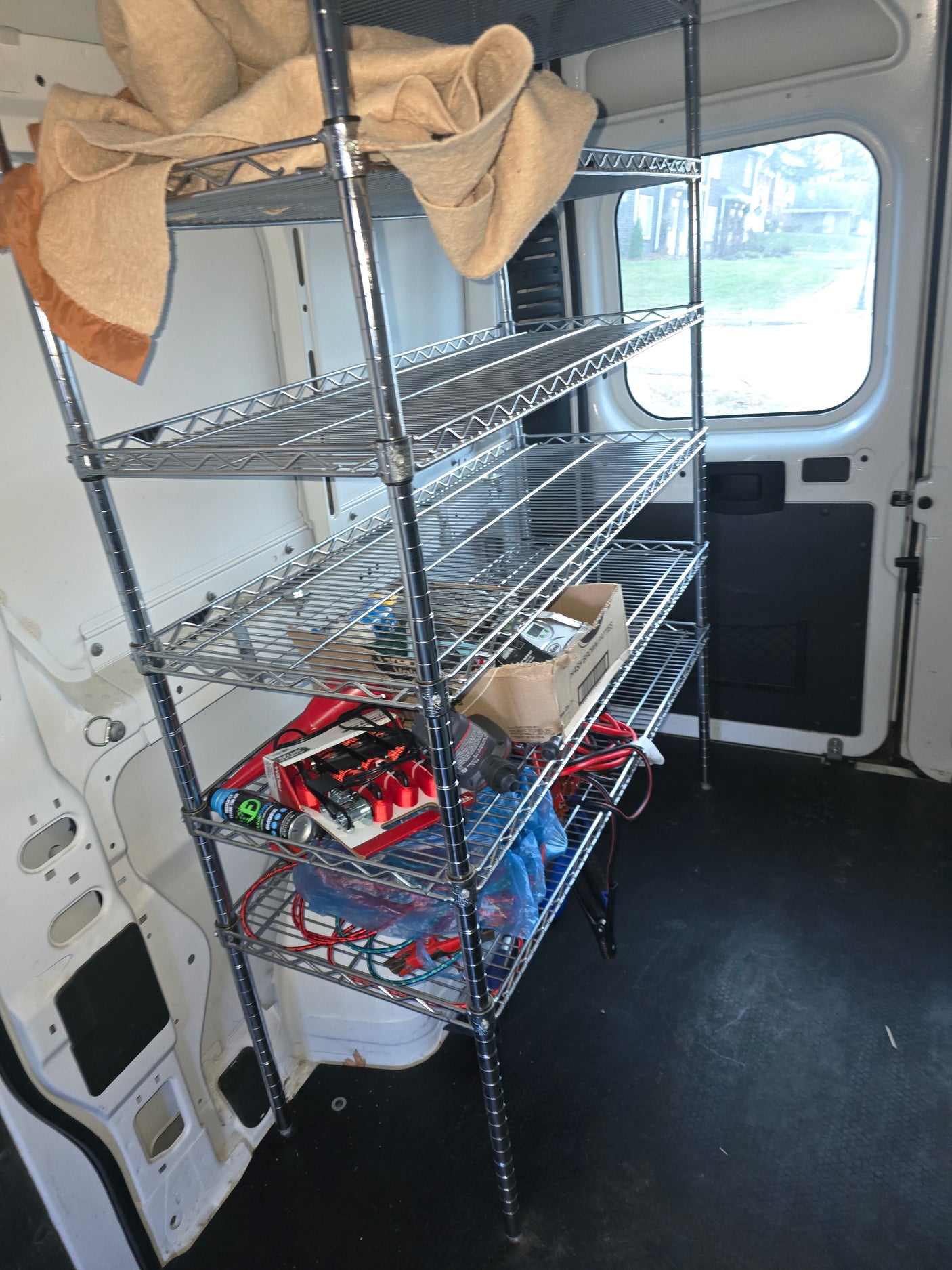 RV rental van interior: chrome wire shelving loaded with blankets, cables, and tools for mobile storage.