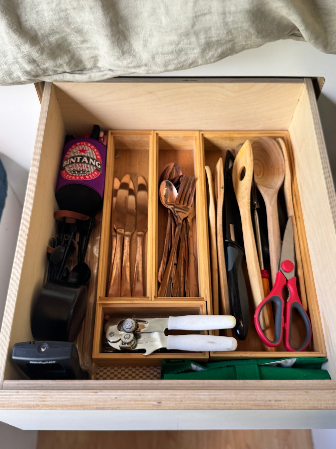 A well-organized RV rental kitchen drawer holds copper and wooden utensils, a can opener, and scissors, maximizing space for travel cooking.