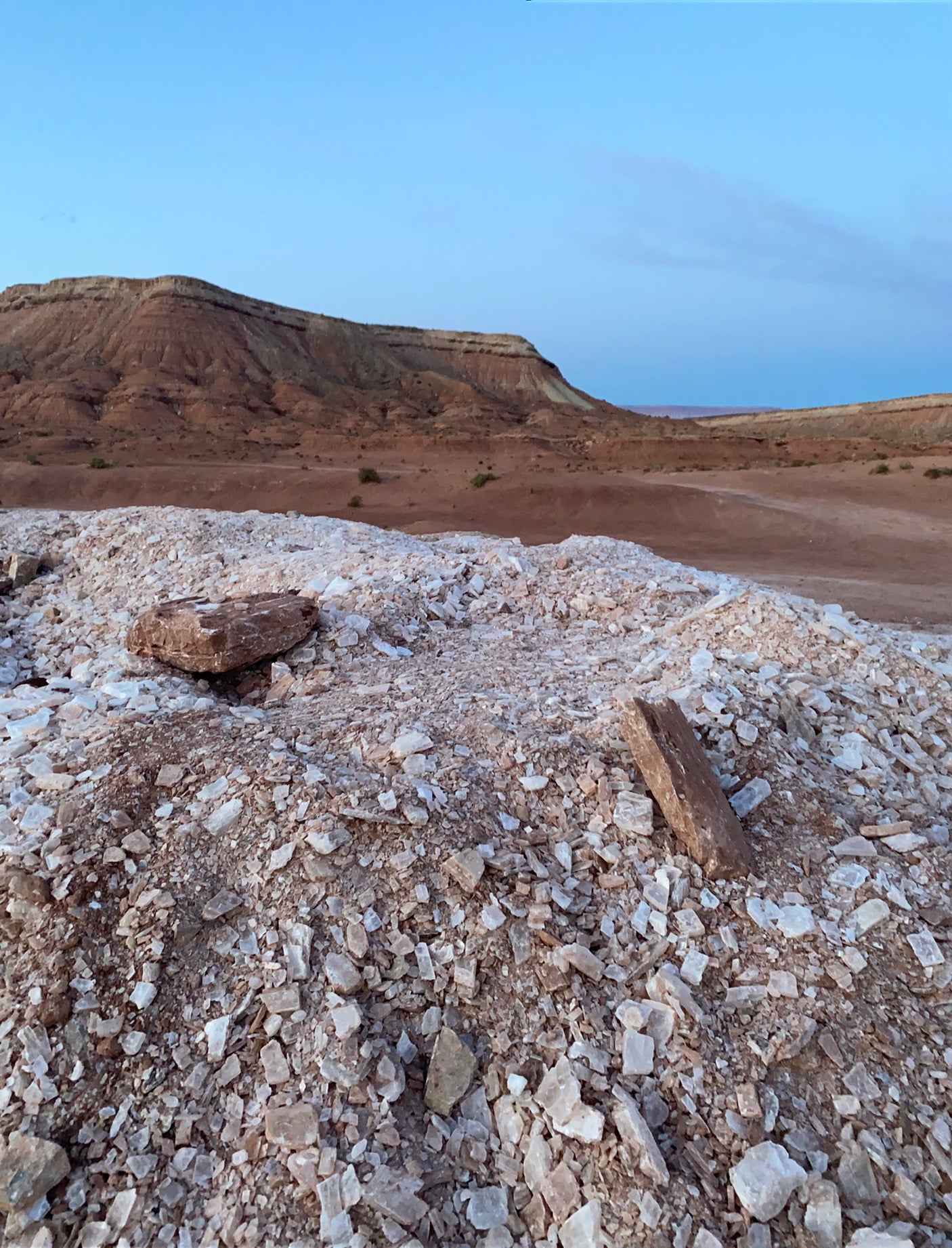 Explore vast desert vistas with an RV rental. Piles of light-colored rocks in the foreground, tiered red hills under a clear sky.