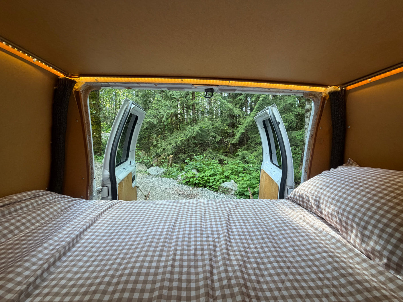 Cozy RV rental bed with an open view to a lush forest from inside. Experience comfortable camping with nature at your doorstep.