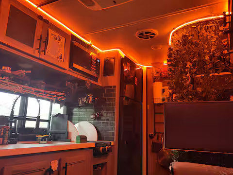 Experience a warm RV rental interior: orange LED lights highlight the compact kitchen & unique plant wall. Adventure awaits!