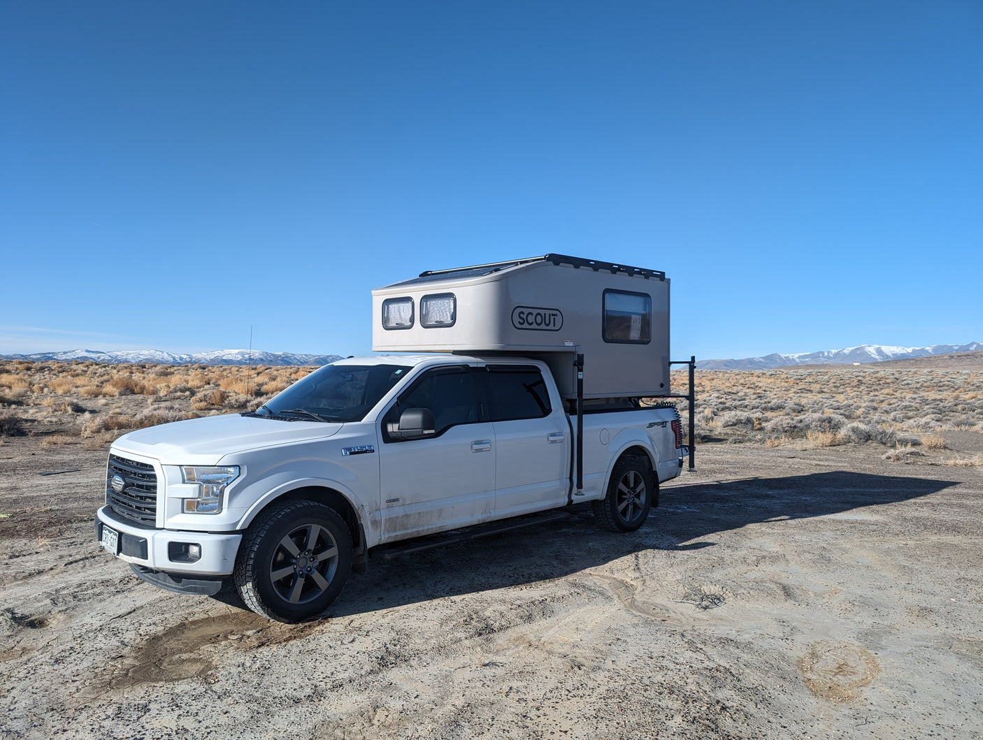 White Ford F-150 with Scout truck camper, an RV rental for off-grid adventures in vast, dry mountain landscapes.