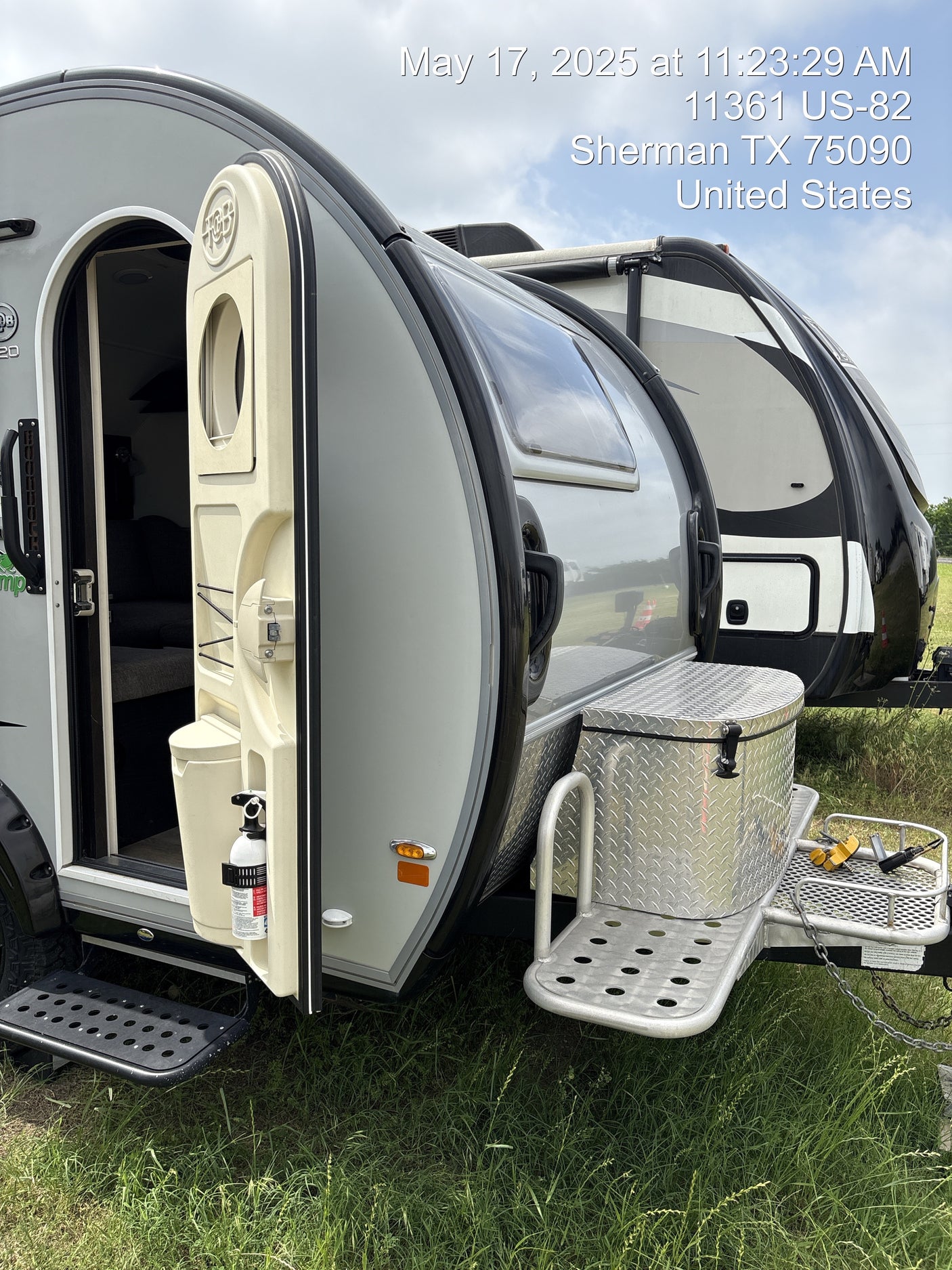 A teardrop travel trailer with an open door, alongside another RV, sitting on grass in Sherman, TX. Explore an RV rental!