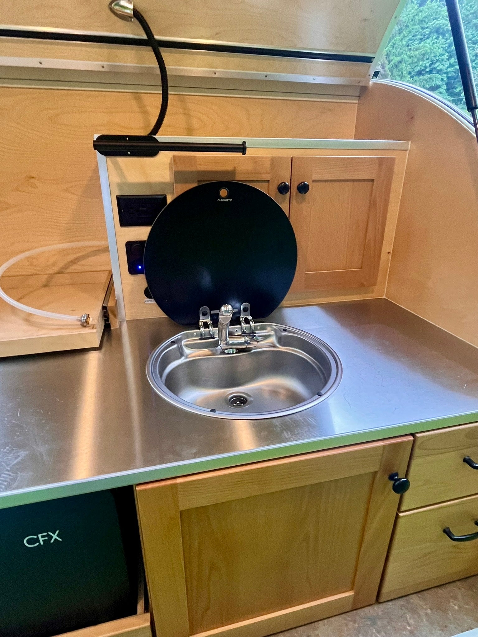 ready for travel.|Compact teardrop RV rental parked in a lush grassy field beside a wooden tiny house