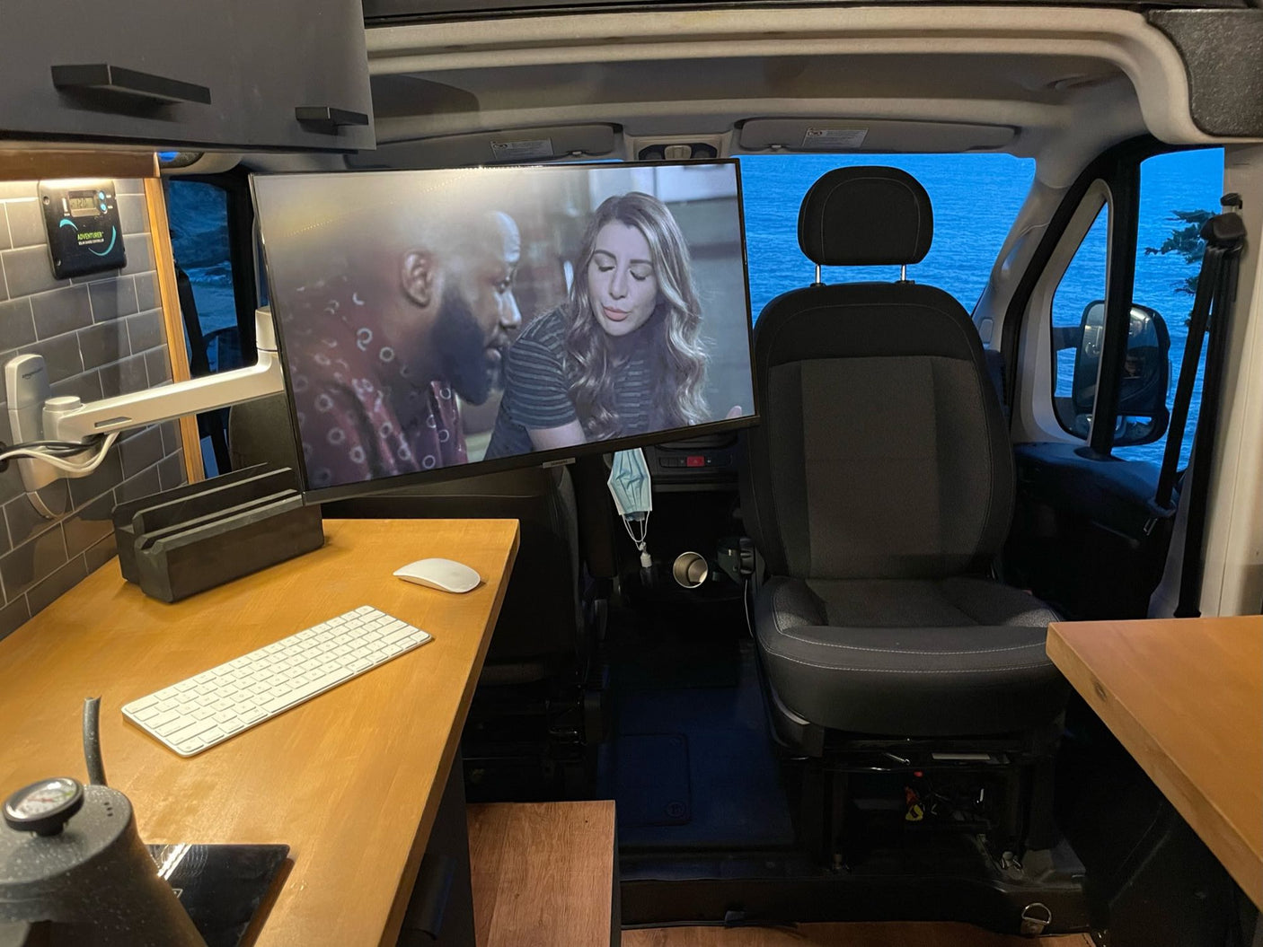Inside an RV rental camper van: A large TV, ergonomic workstation, and scenic ocean views combine for a comfortable mobile office.