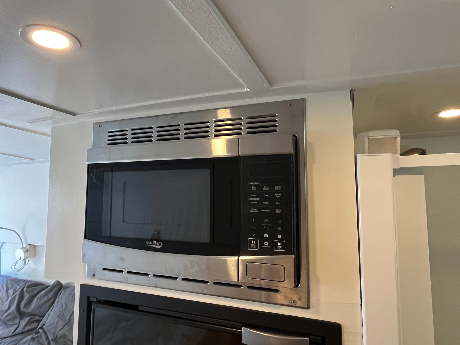 A High Pointe stainless steel microwave oven, mounted in an rv rental. It features a digital control panel and is situated under ceiling lighting.