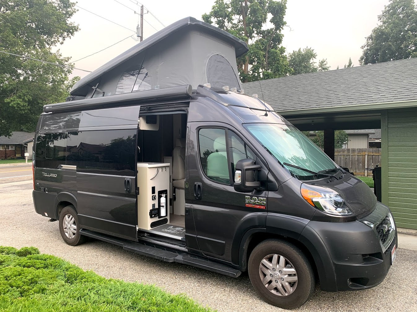 Dark gray RAM ProMaster pop-top RV rental with side door open, showcasing its outdoor kitchen unit.