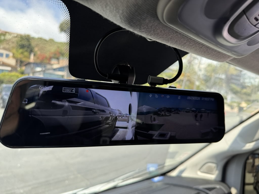 Digital rearview mirror in an RV rental, displaying a split screen view: a front vehicle perspective and a beach scene.