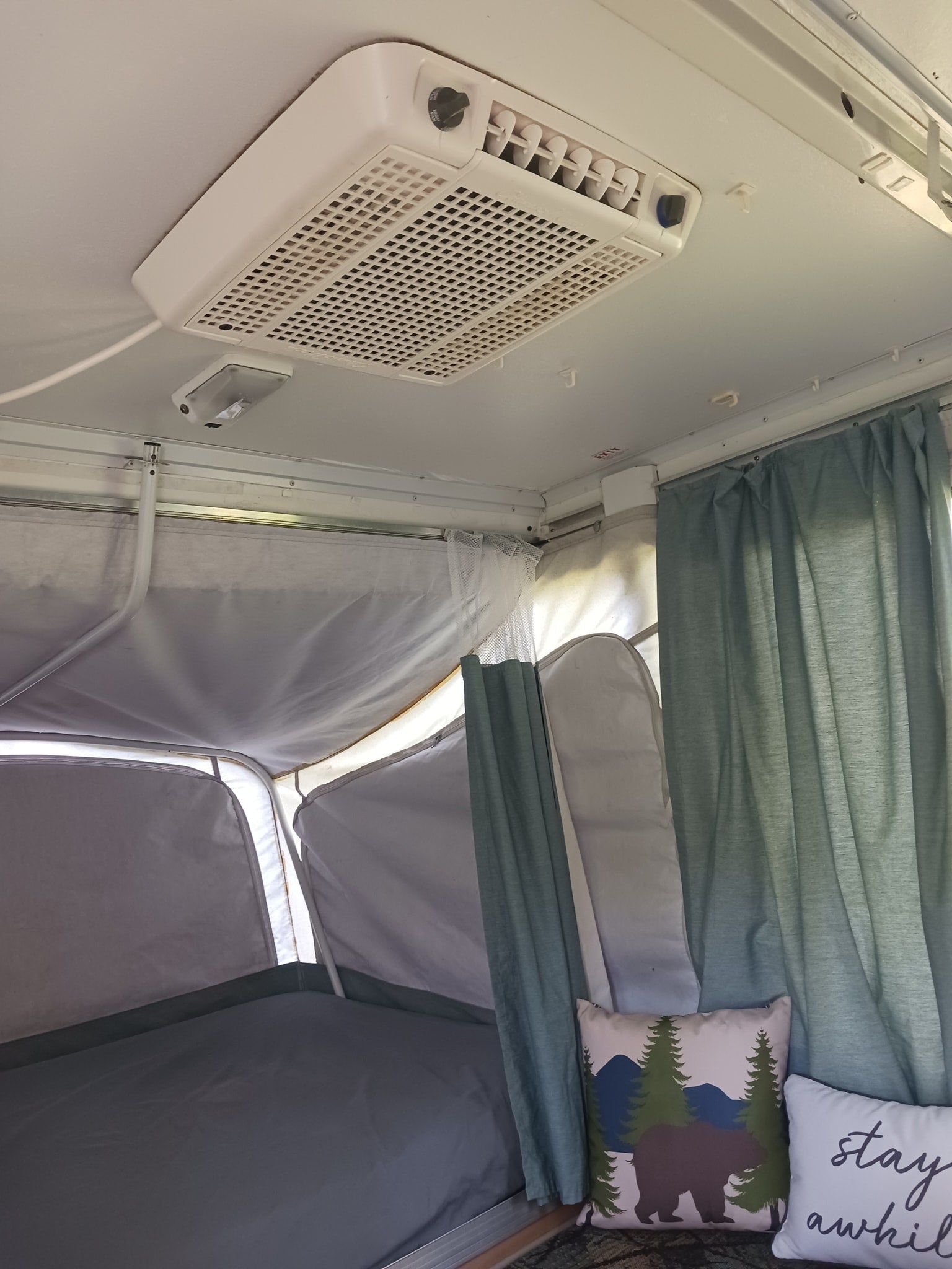 Cozy RV rental interior. Pop-up camper bedroom with a ceiling AC unit, comfy bed, and inviting pillows.
