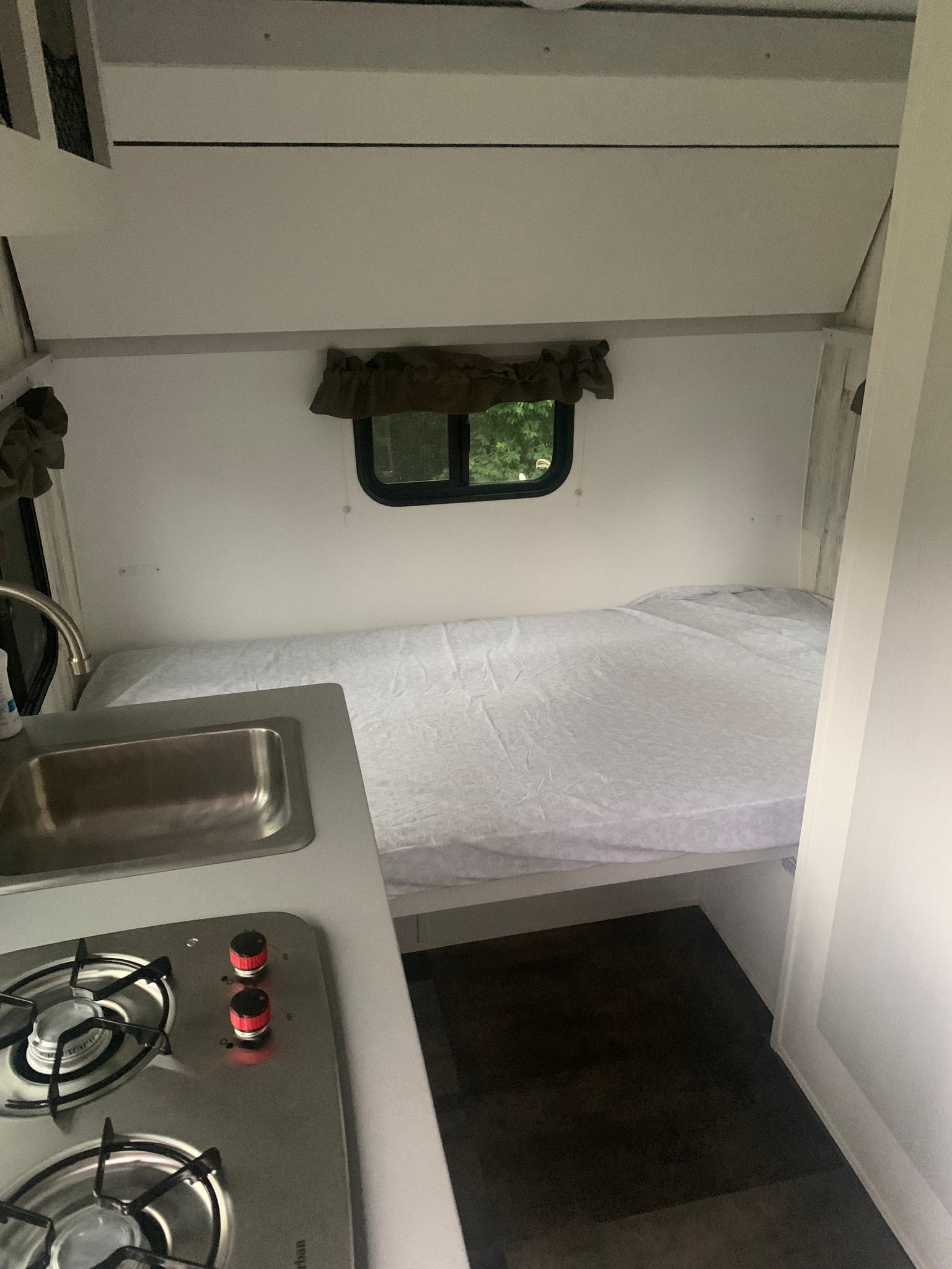 Compact RV rental interior featuring a comfy bed, window with nature views, and a small kitchen with sink and stovetop.