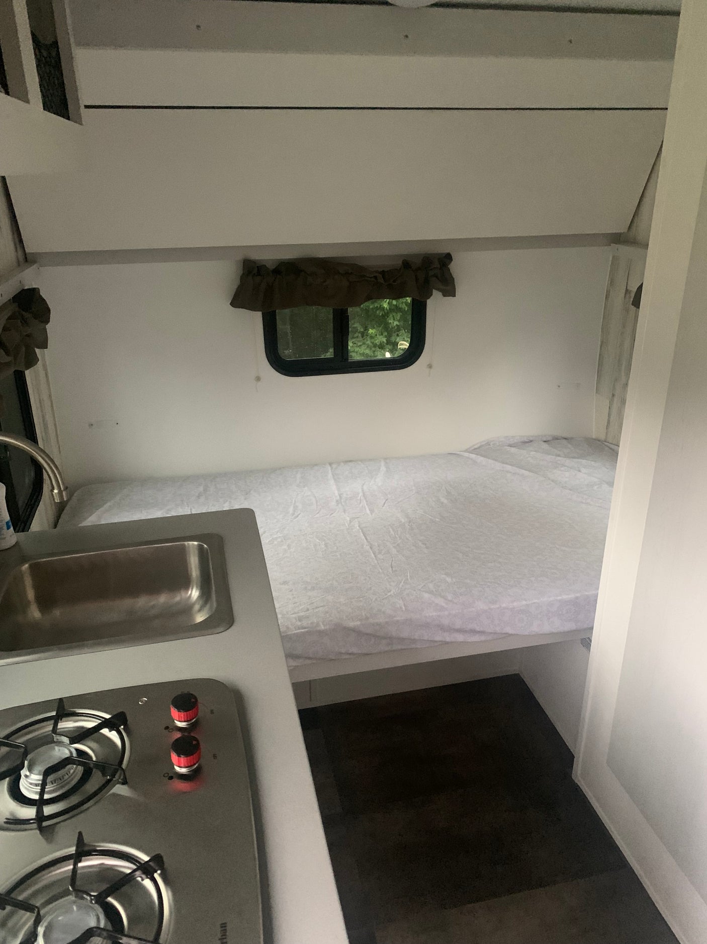 Compact RV rental interior featuring a comfy bed, window with nature views, and a small kitchen with sink and stovetop.