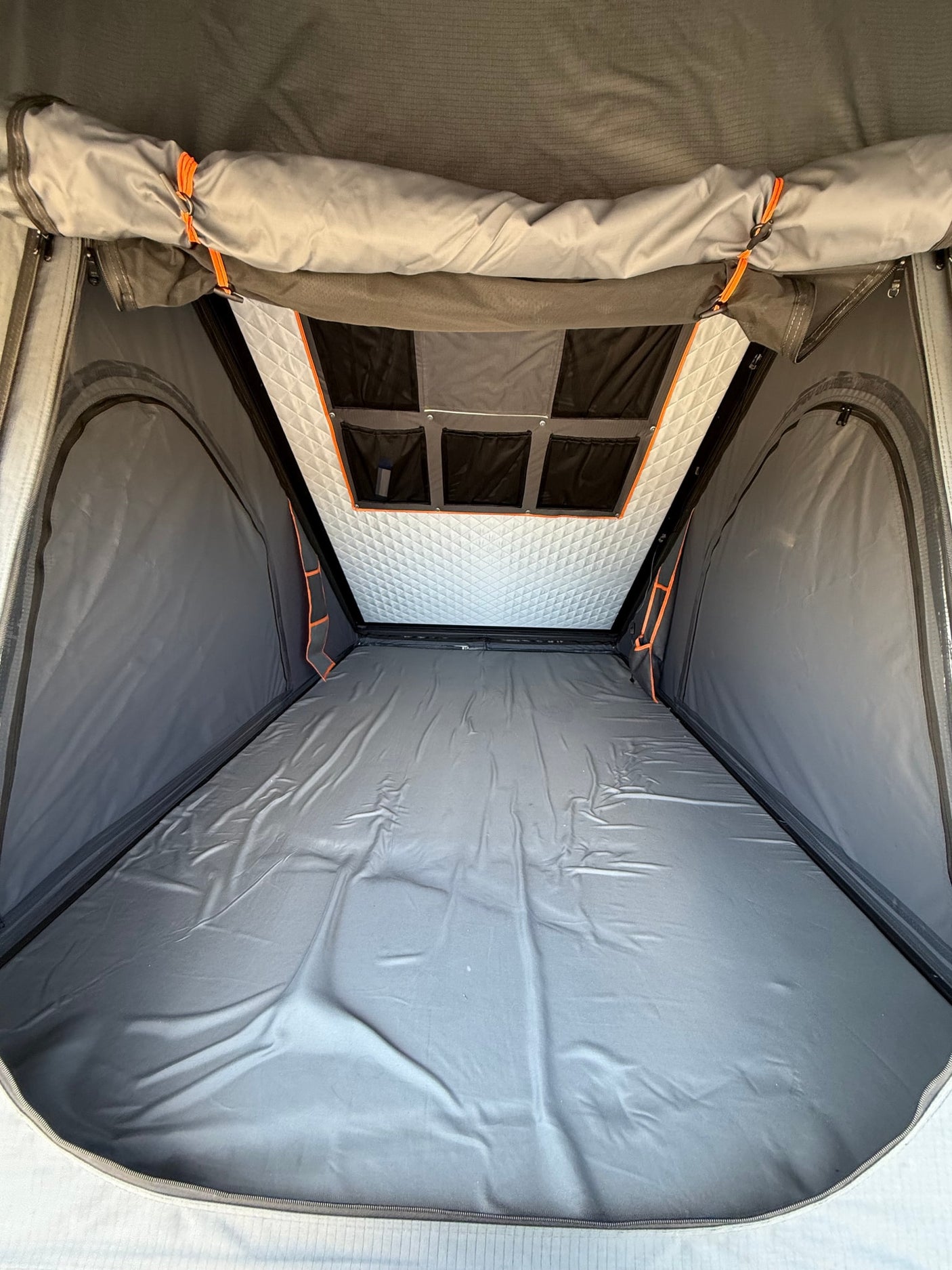 Interior view of an RV rental rooftop tent, featuring a grey sleeping area, quilted ceiling, and storage pockets.