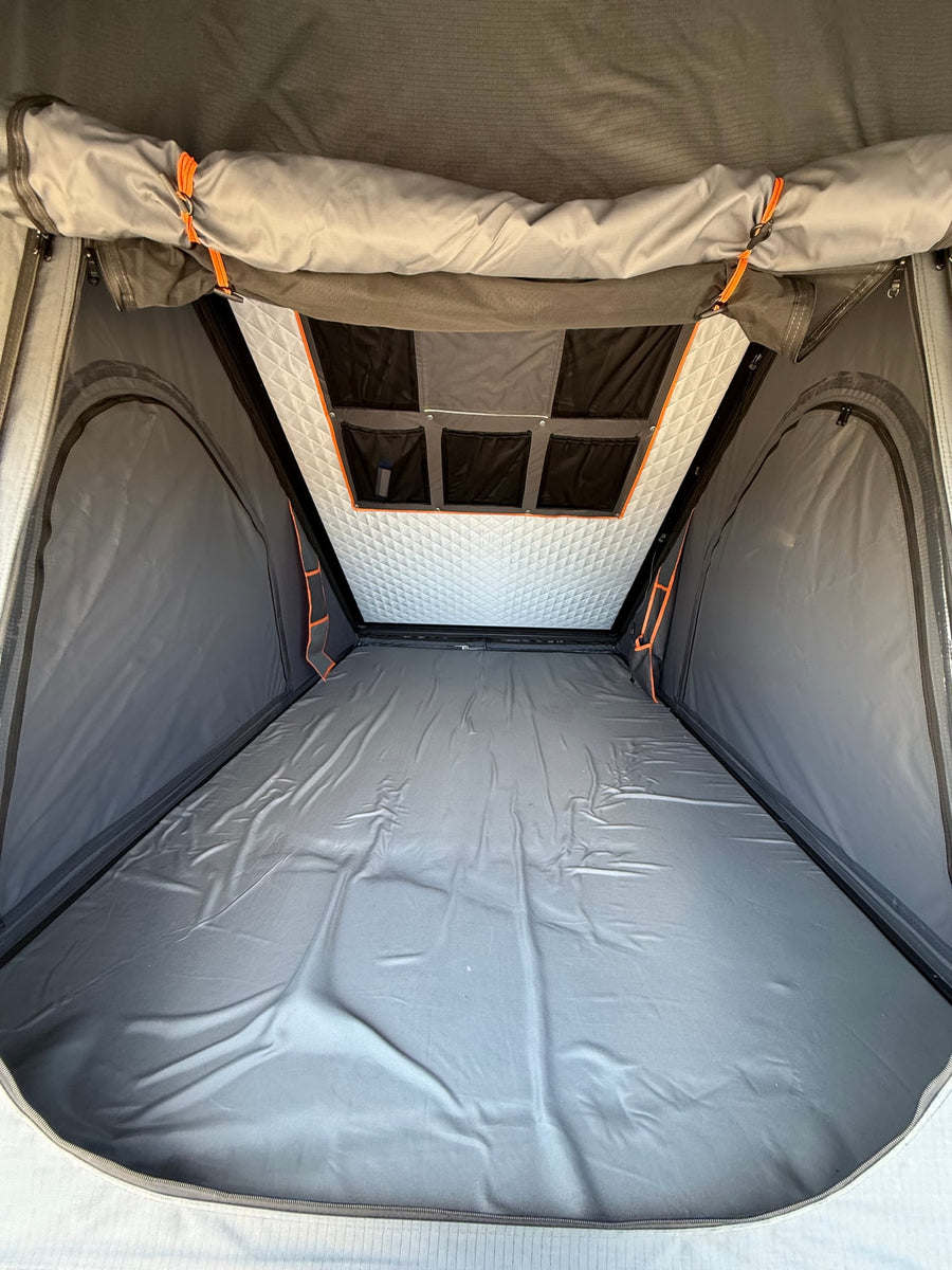 Interior view of an RV rental rooftop tent, featuring a grey sleeping area, quilted ceiling, and storage pockets.