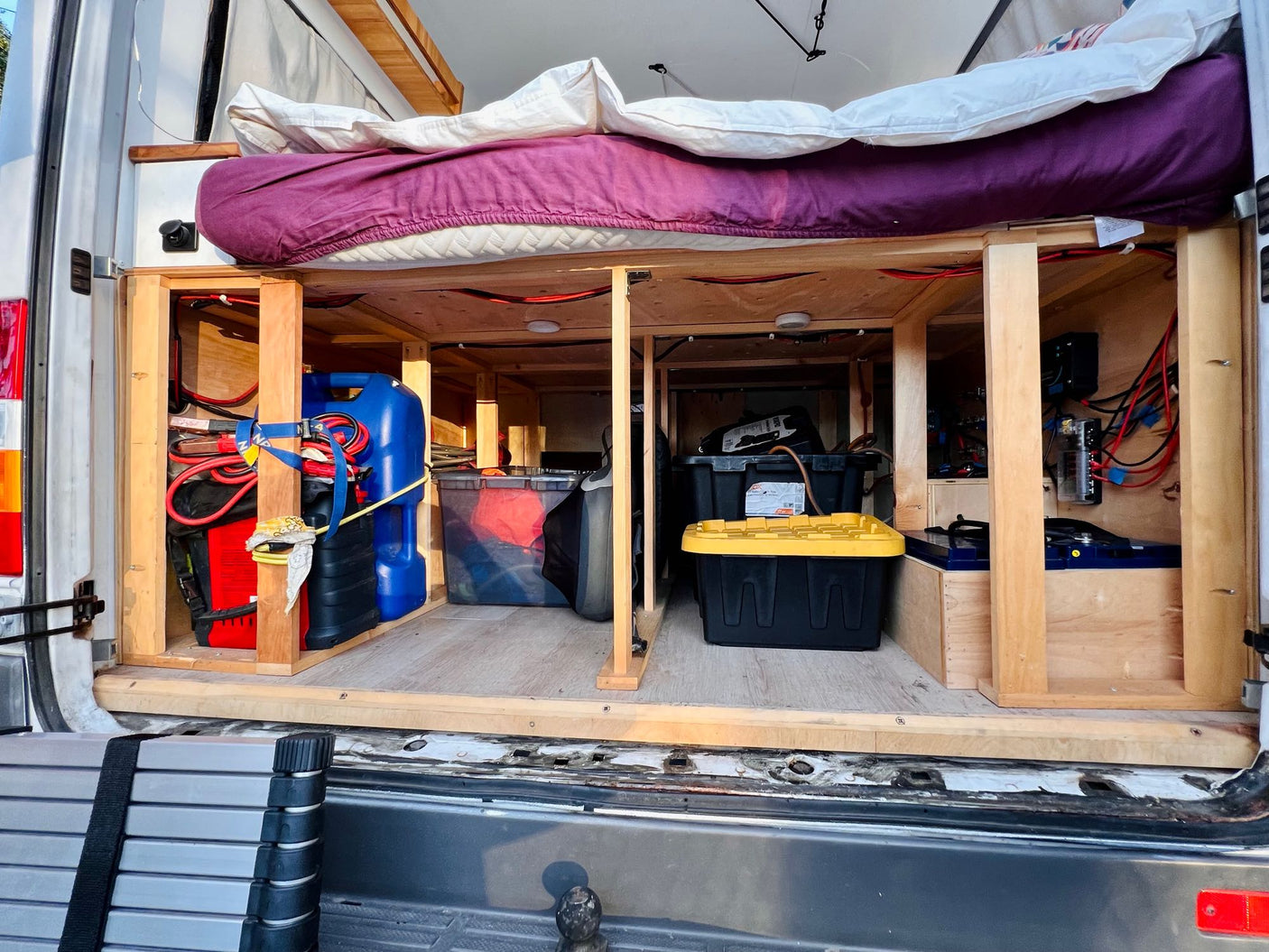 Organized camper van storage & power setup for an RV rental. Under-bed area shows utilities, bins, and electrical system.