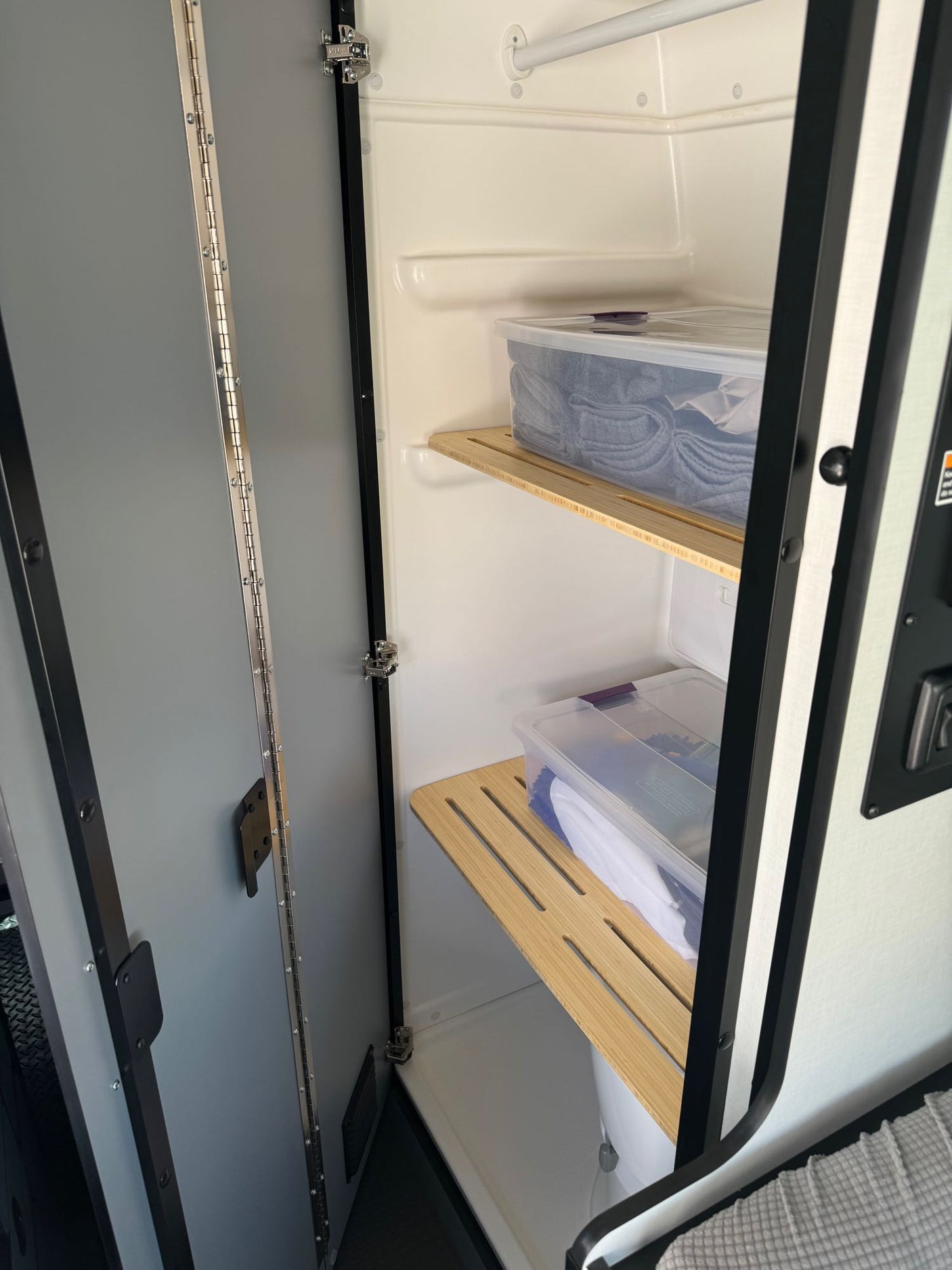 RV rental shower stall converted to storage with slatted shelves holding clear bins of towels and supplies, maximizing space.