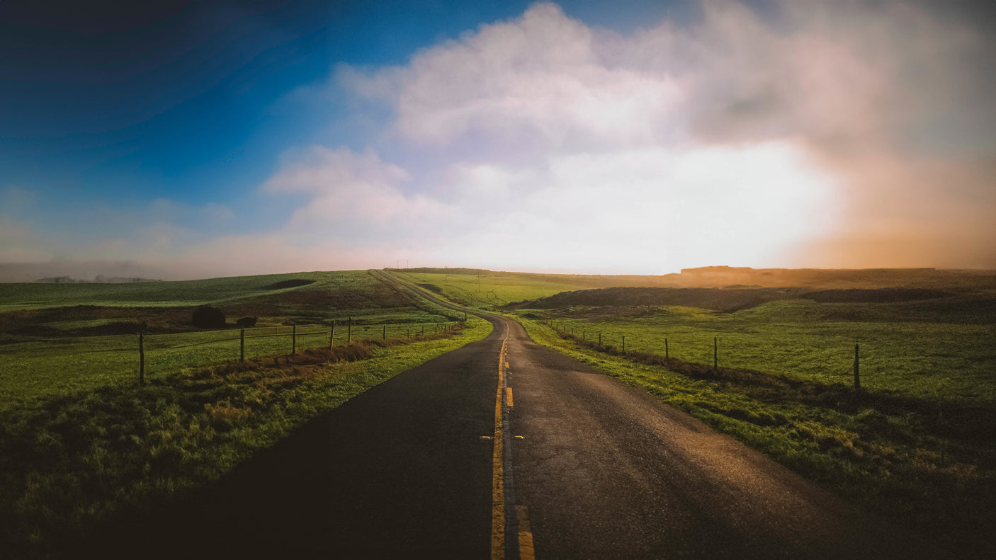 Scenic road winding through green fields under a hazy sky, perfect for an RV rental road trip.