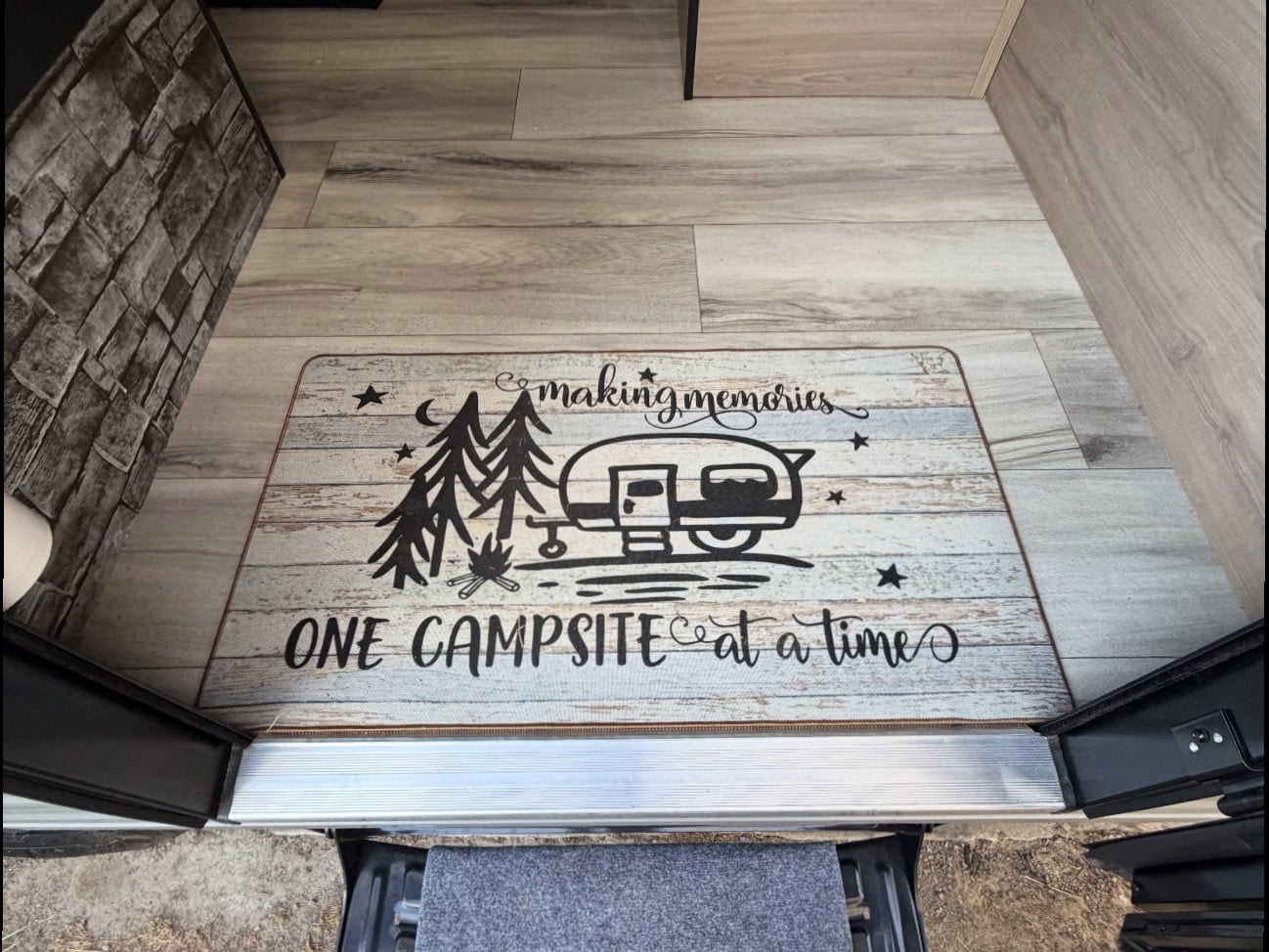 featuring an extended awning with LED lights and a meal cooking on a portable stove.|Welcome to your RV rental! A doormat inside the entrance reads 'making memories ONE CAMPSITE at a time' with camping graphics.|Step inside this inviting rv rental! Features include a compact kitchen — photo 2