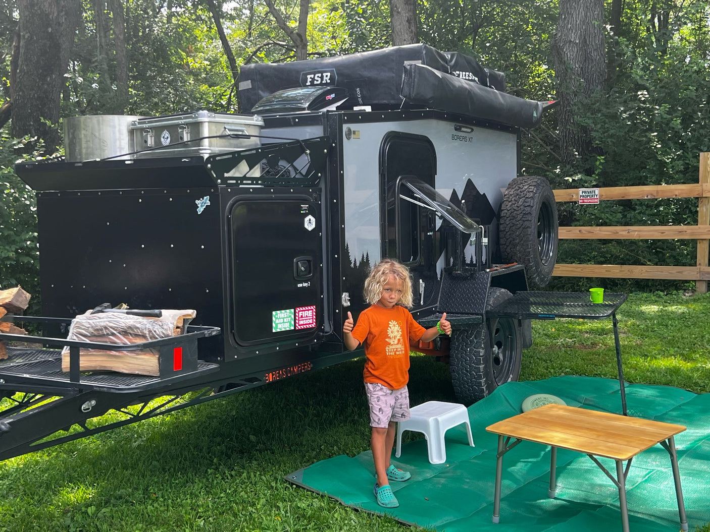 A happy child gives thumbs up next to a rugged Boreas XT camper trailer, ready for an adventure. Perfect for RV rental exploration!