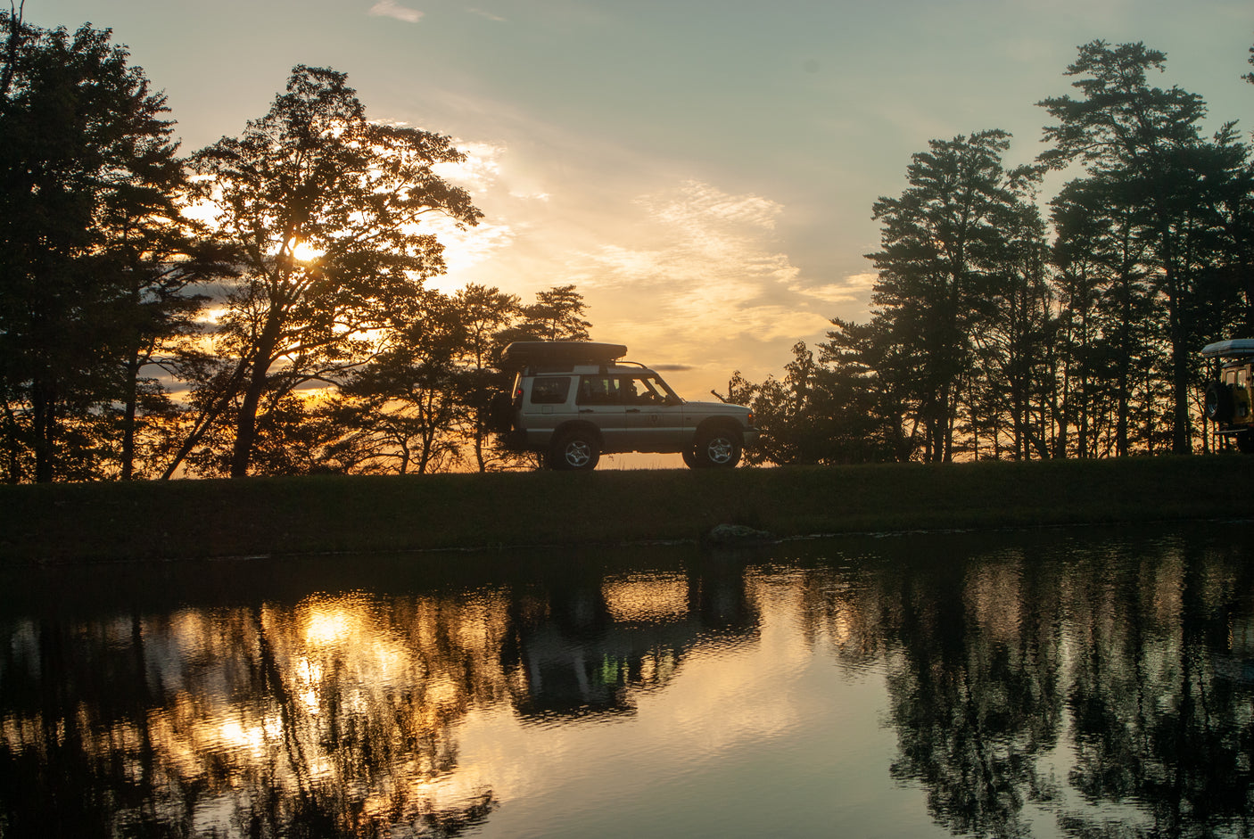 An adventure-ready SUV, perfect as an RV rental, stands by tranquil water at golden hour with silhouetted trees.