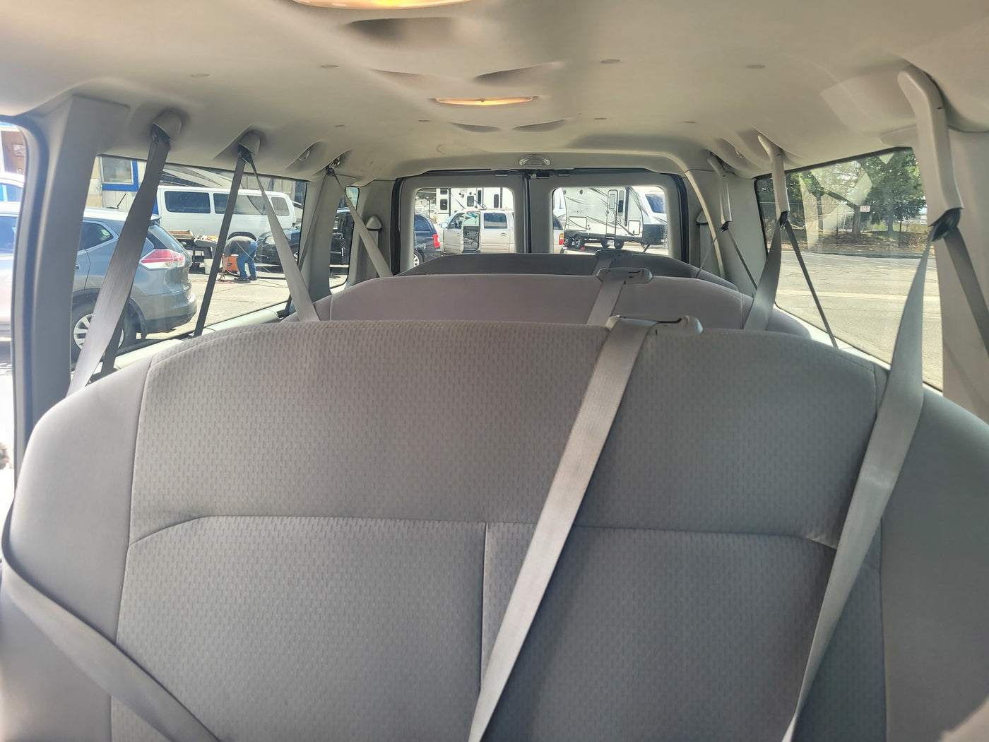 View from inside an RV rental van showing three rows of grey seats and seatbelts, with RVs outside in a sunny parking lot. — photo 5