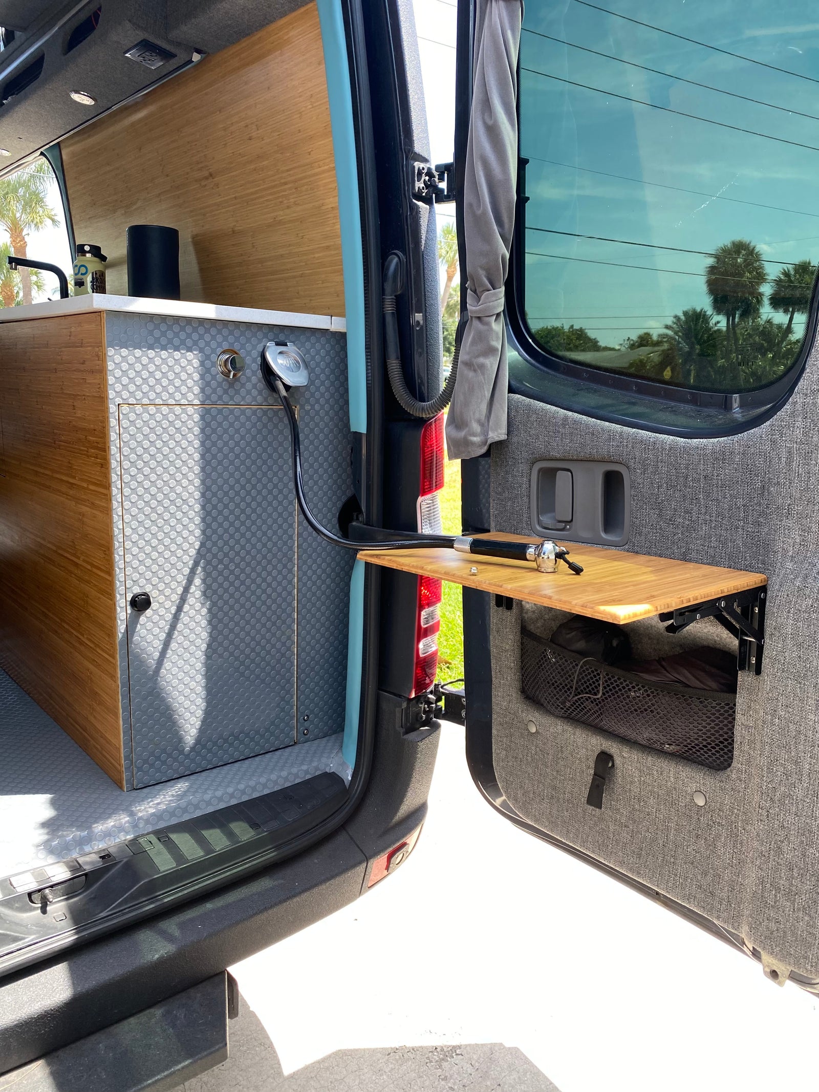 RV rental with functional interior: bamboo kitchen, sink, and outdoor shower setup on rear door table for convenient use.