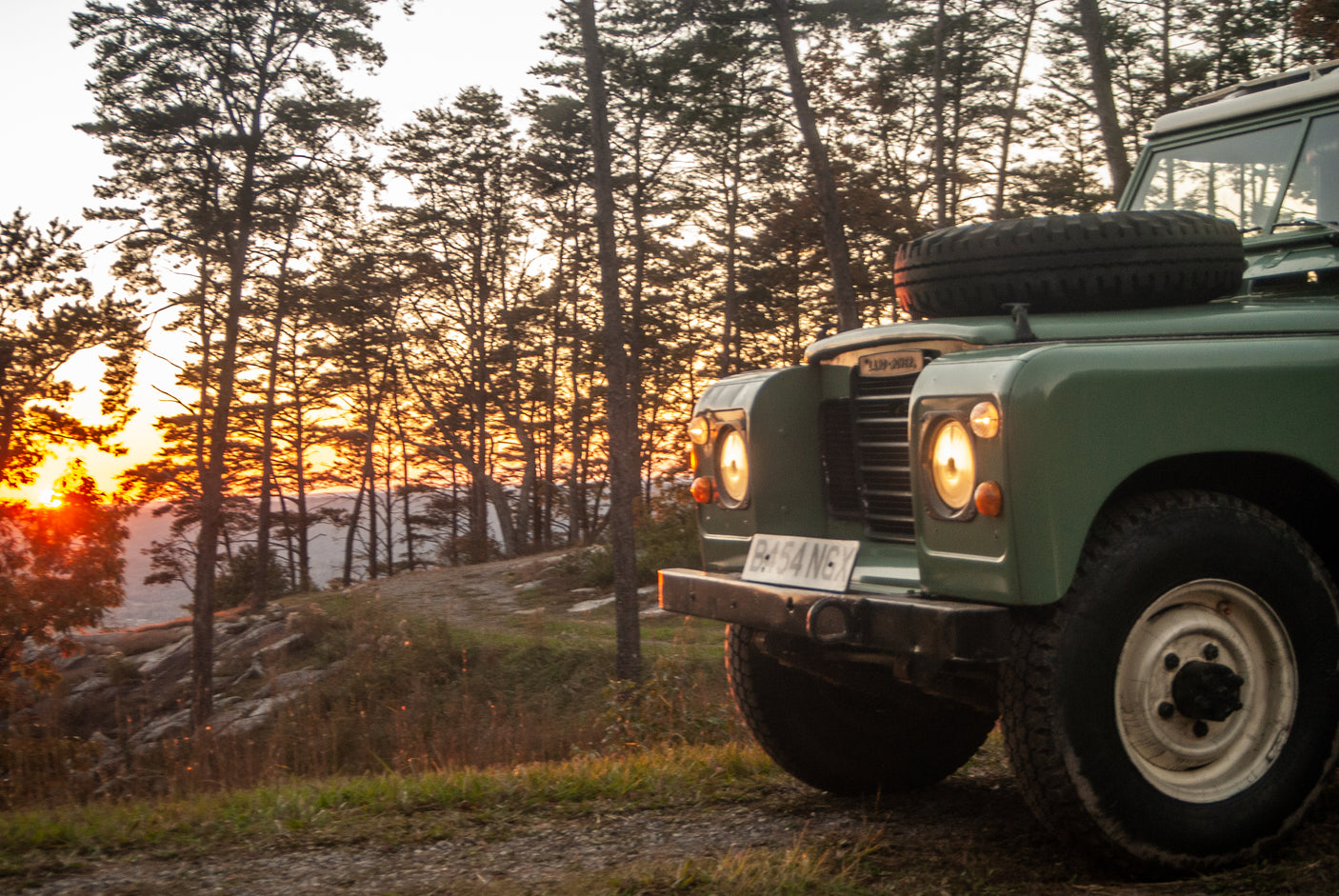A rugged green Land Rover on a dirt road at sunset, perfect for off-road trips. Find your next adventure, whether it's this or an **RV rental**.
