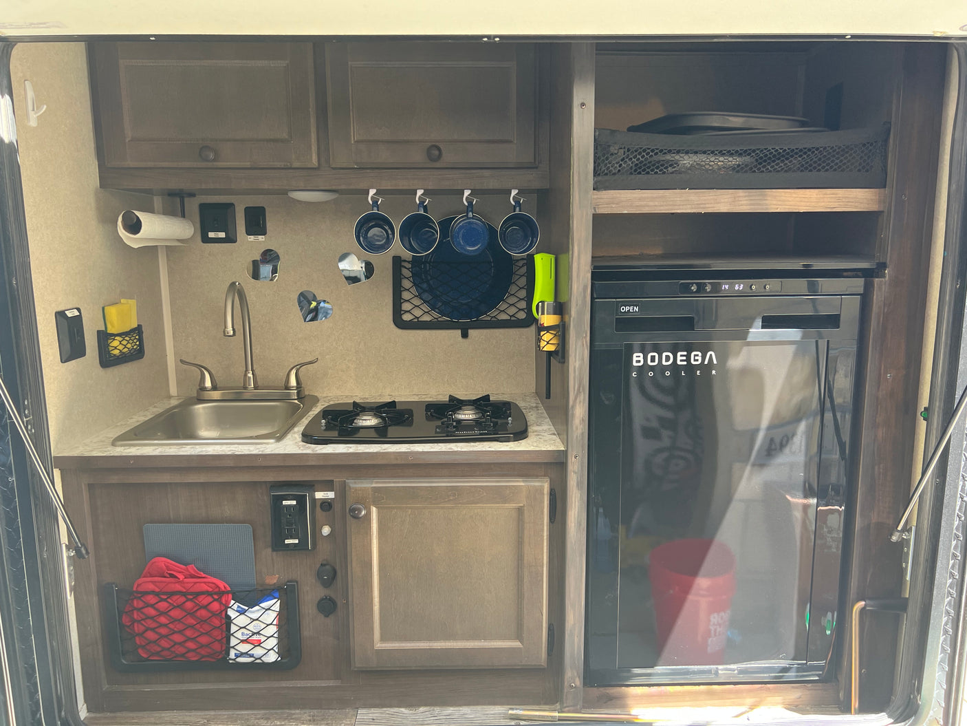 Inside an rv rental, a compact kitchen features a sink, two-burner stove, refrigerator, and smart storage solutions.