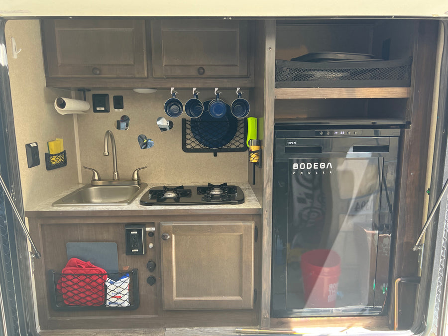 Inside an rv rental, a compact kitchen features a sink, two-burner stove, refrigerator, and smart storage solutions.