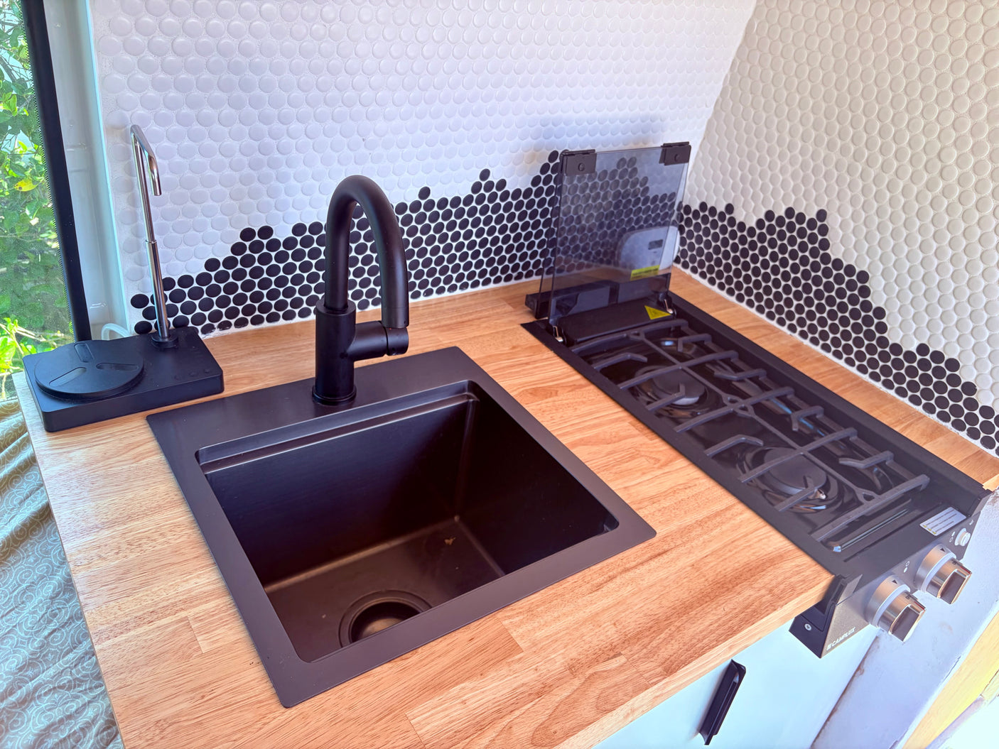 This RV rental features a modern kitchenette with a black sink, faucet, gas stove, wood counter, and unique penny tile backsplash.